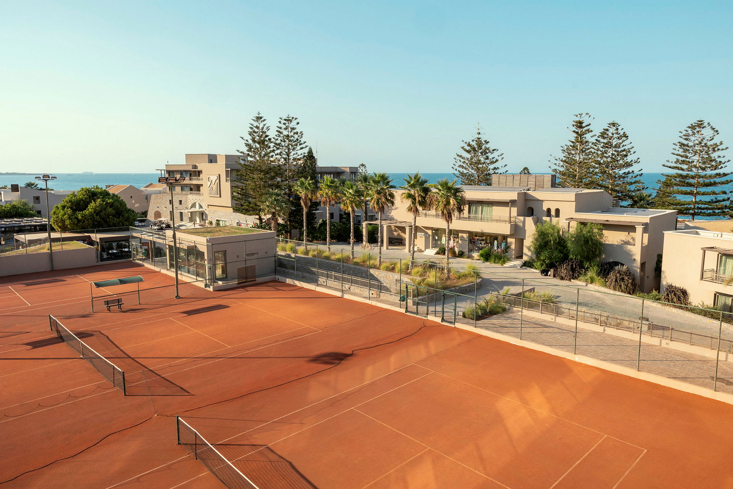 En öppen tennisbana med en byggnad och havet i bakgrunden. (AI-genererad text)