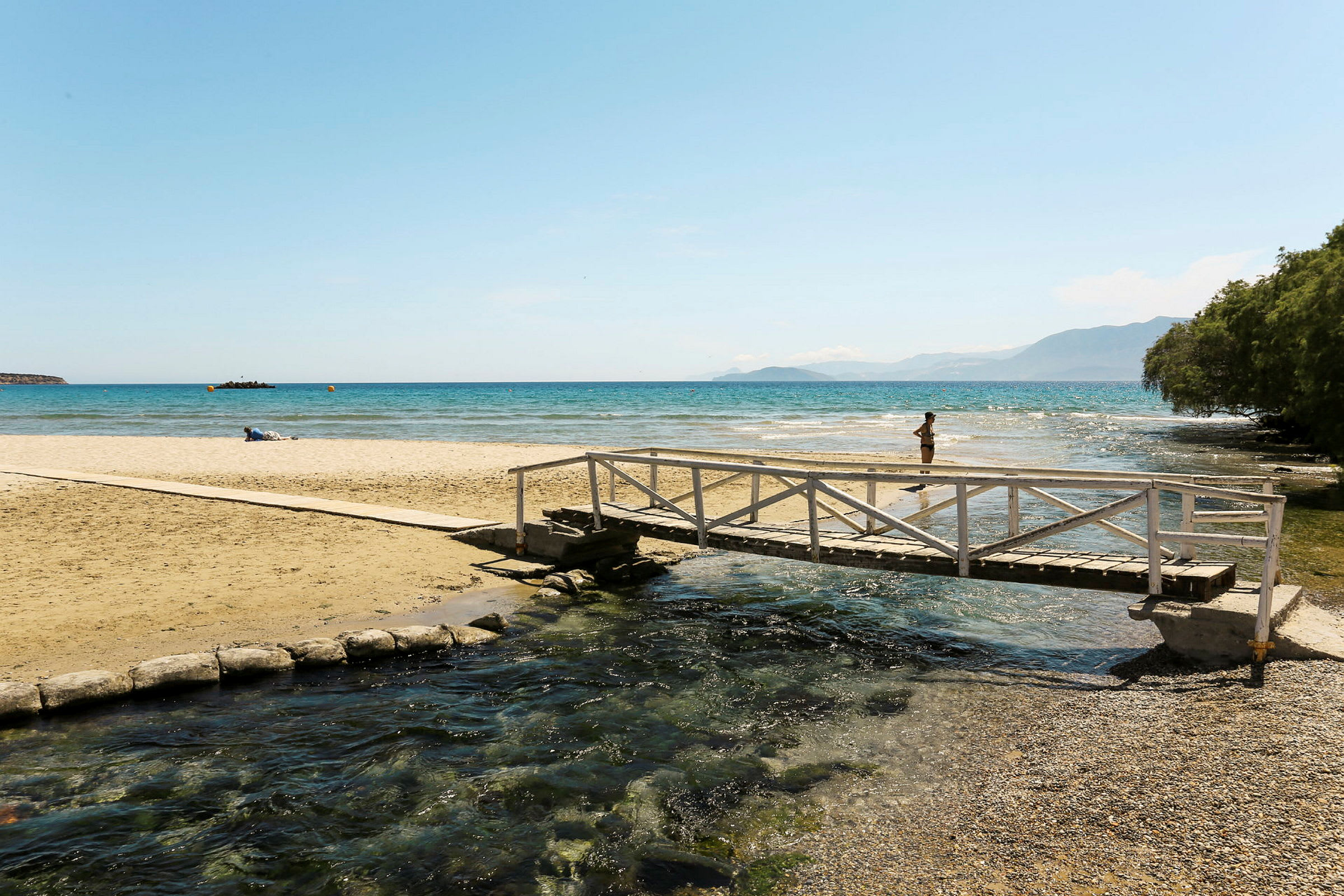 En sandstrand med ett träbro över en ström, och havet i bakgrunden. (AI-genererad text)