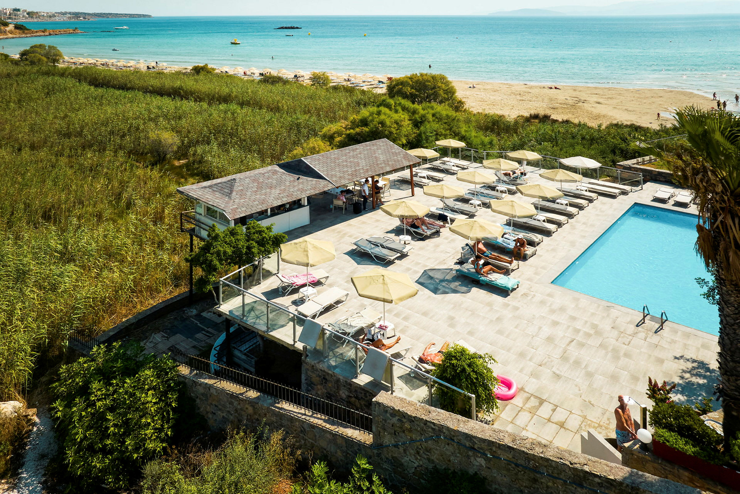 Utsikt över en pool längs en strand med parasoller och solstolar. (AI-genererad text)