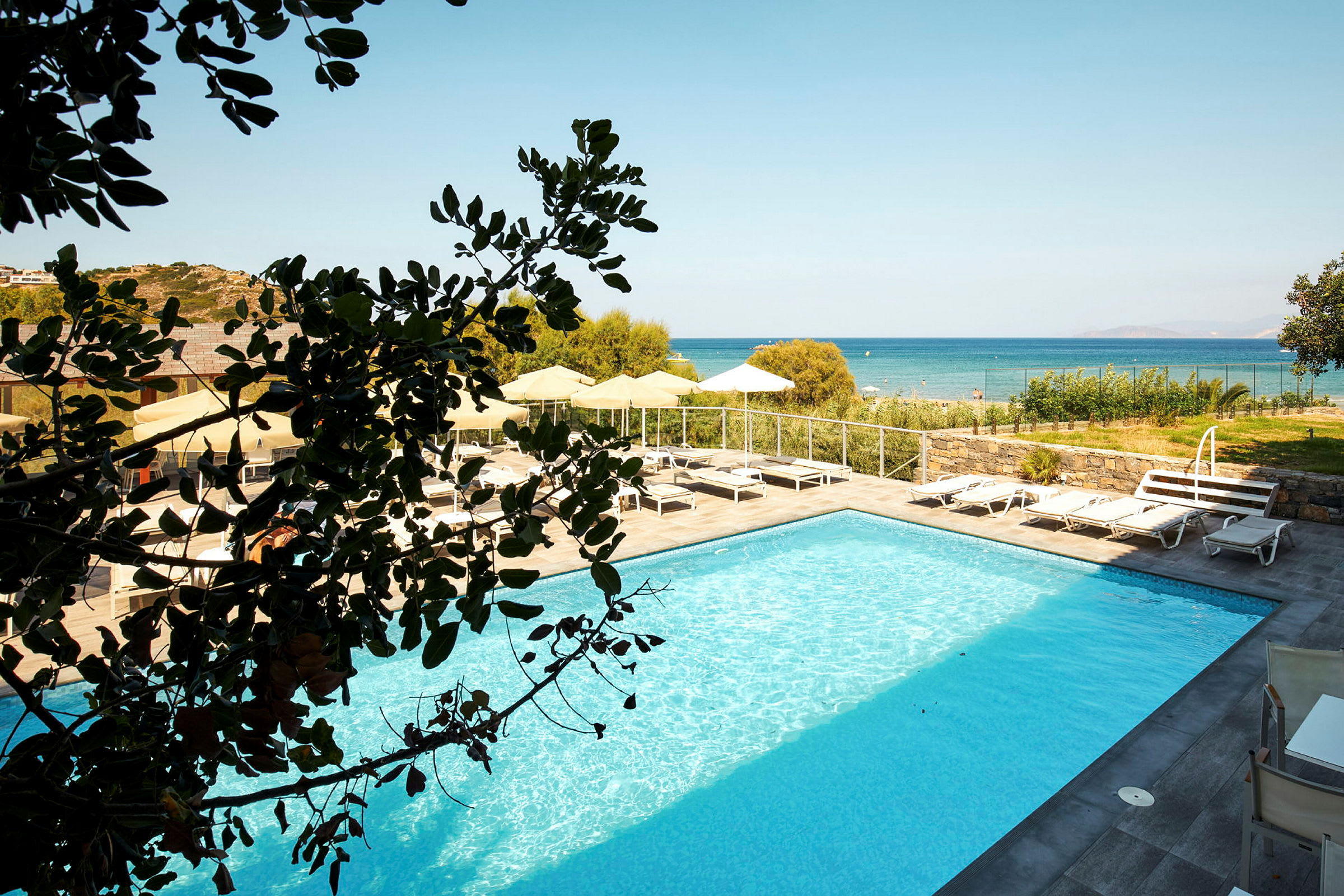 Utsikt över en pool med solstolar, parasoller och havet i bakgrunden. (AI-genererad text)