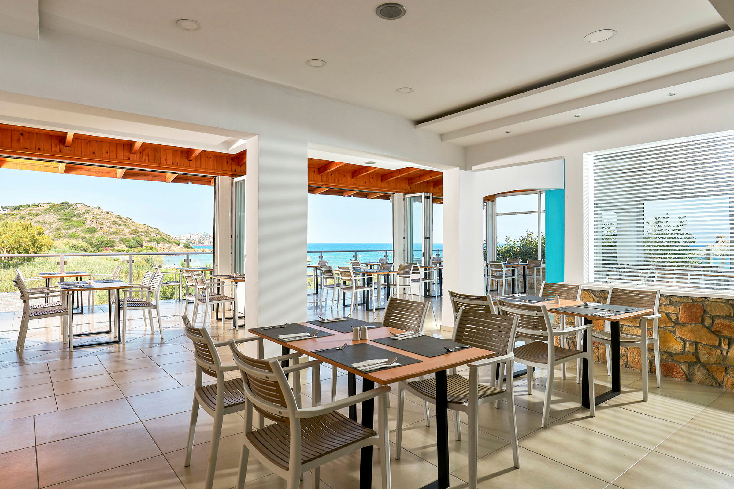 En restaurang med utsikt över havet, med bord och stolar inomhus och på en terrass. (AI-genererad text)