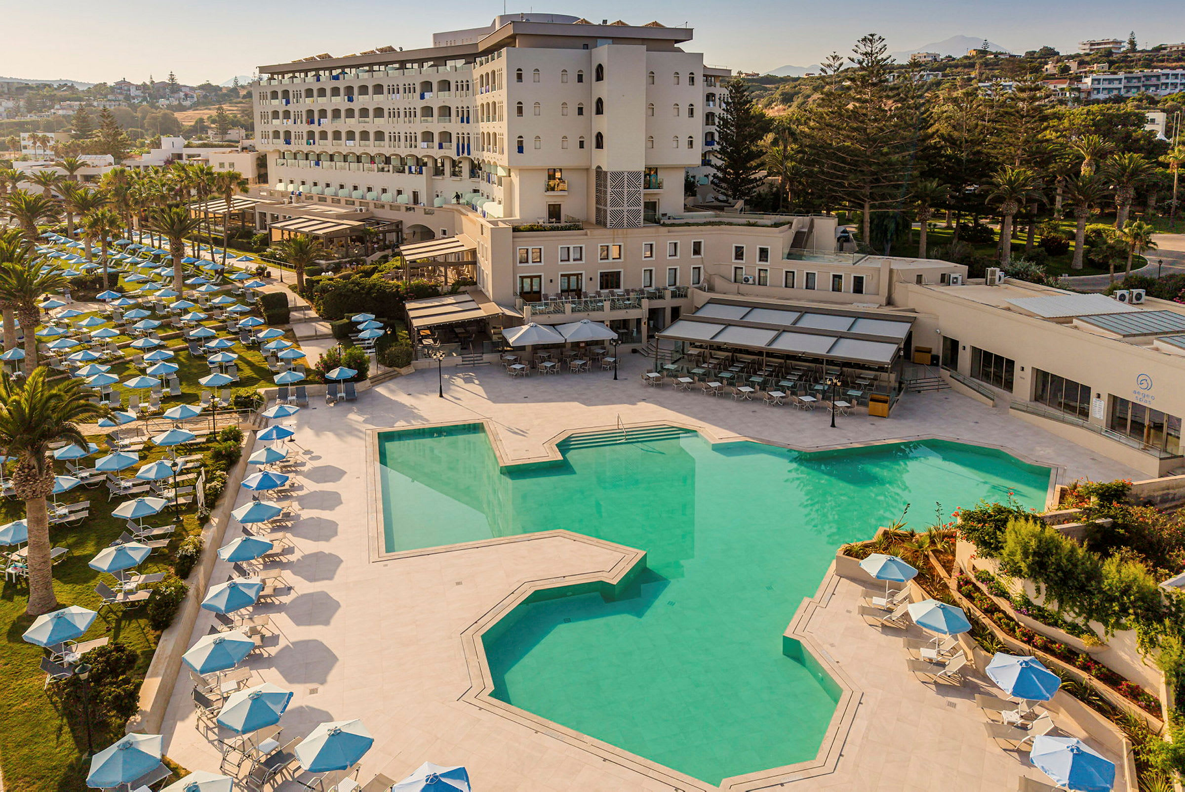 Bild av ett hotell med en stor utomhuspool och många solstolar med parasoller på gräsmattan vid poolområdet. (AI-genererad text)