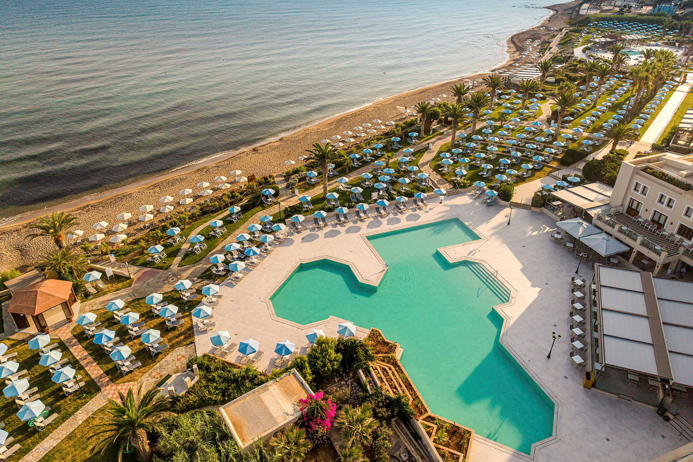 Bild av en resort med en stor pool omgiven av solsängar och parasoller. Stranden med solstolar och parasoller syns nära havet. (AI-genererad text)