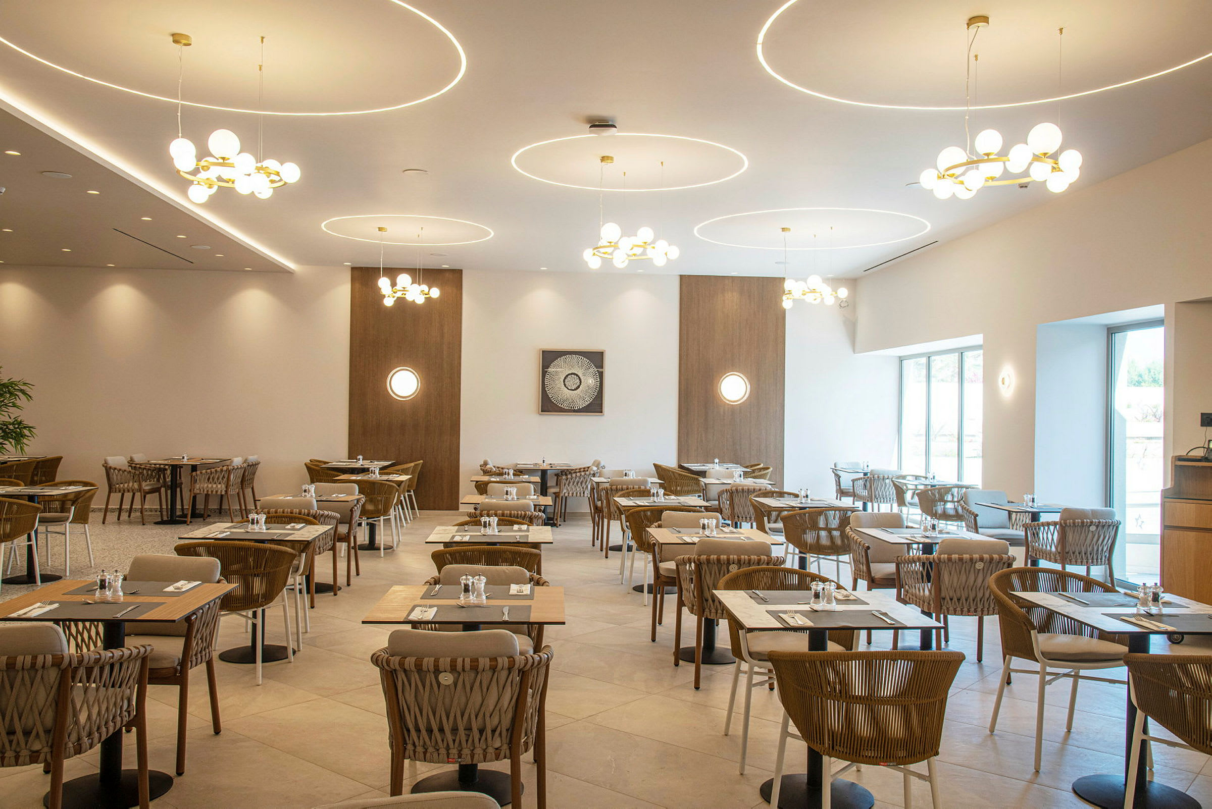 En restaurang med moderna möbler och dekor, dukade bord och stolar. Ljuskronor hänger från taket. (AI-genererad text)