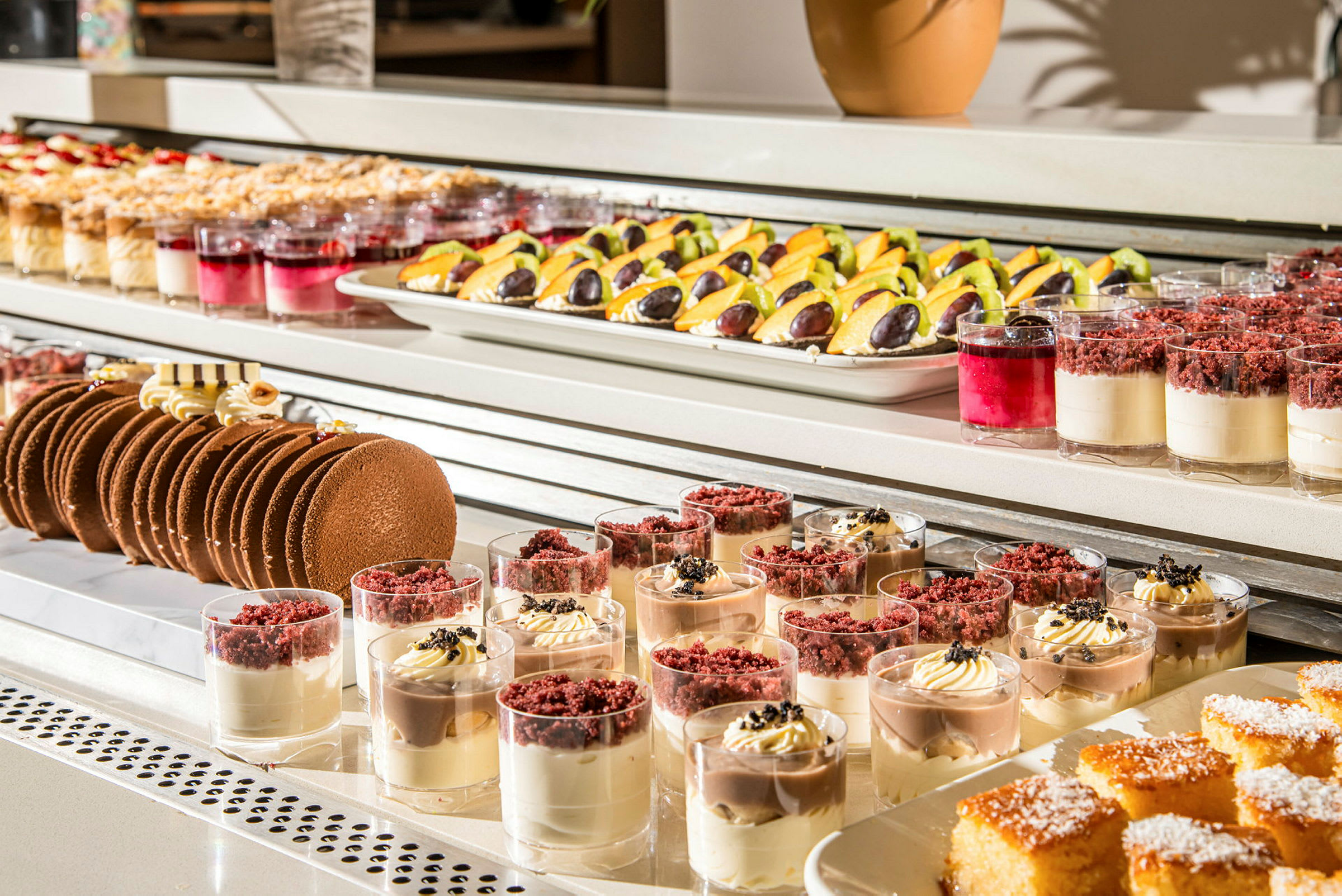 Bilden visar en buffé med olika desserter, inklusive små desserter i glas, kakor och fruktgarnityrer. (AI-genererad text)