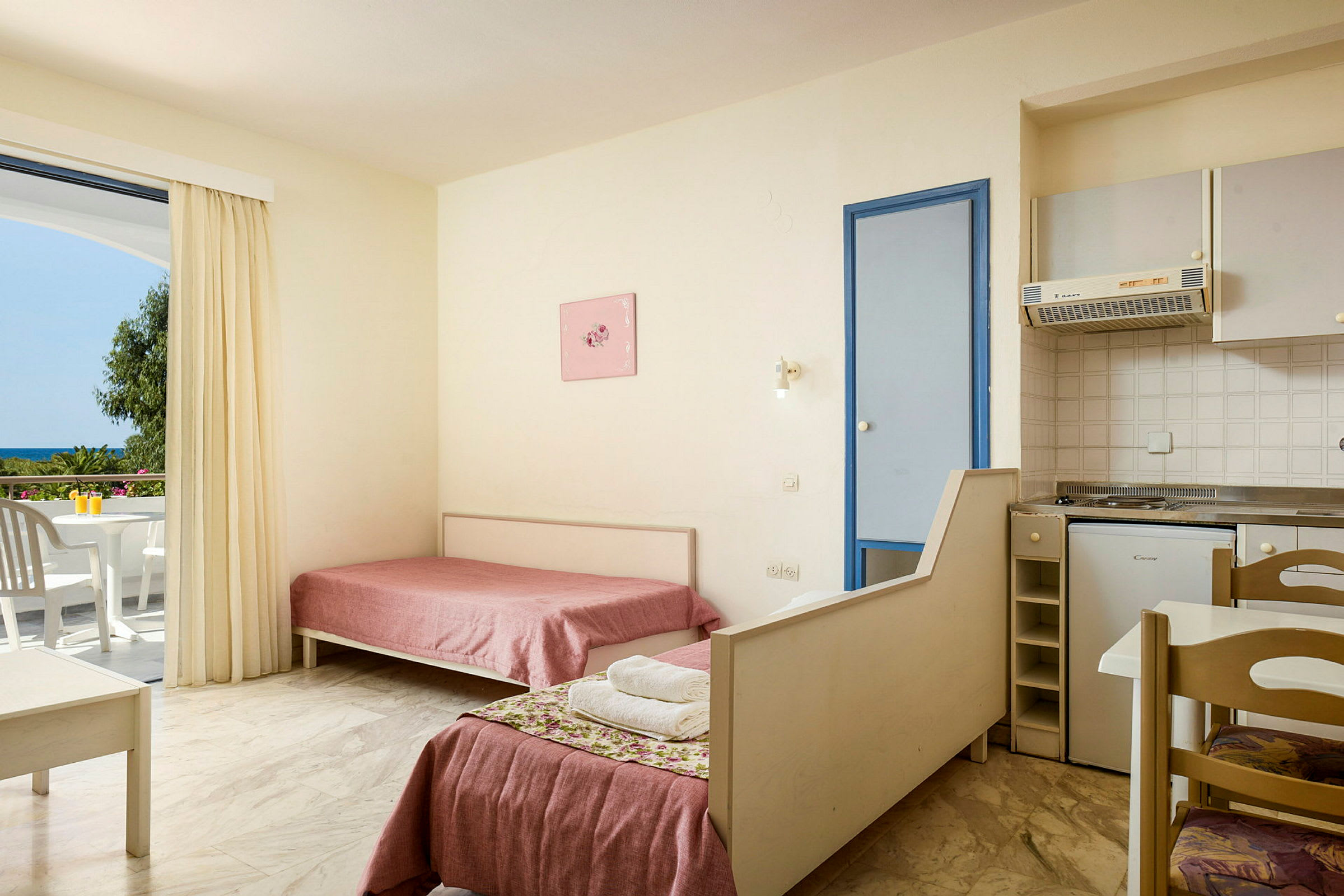 Interiör av ett hotellrum med två enkelsängar, ett litet kök och en balkong med utsikt. (AI-genererad text)
