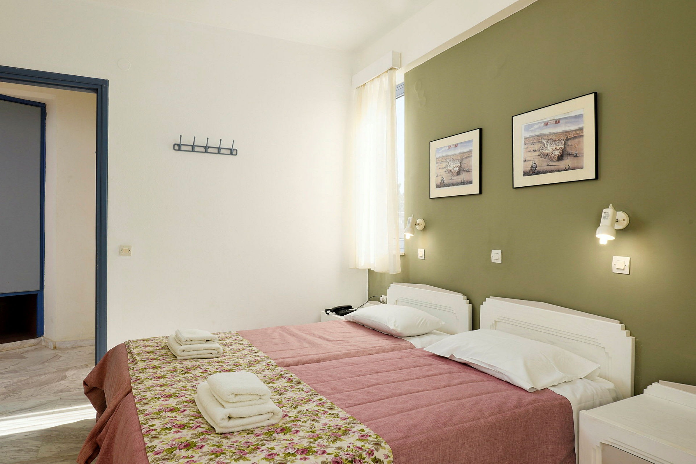 Ett hotellrum med två enkelsängar bäddade med rosa täcke och blommönstrade överkast. På väggen hänger två tavlor ovanför sängarna. (AI-genererad text)
