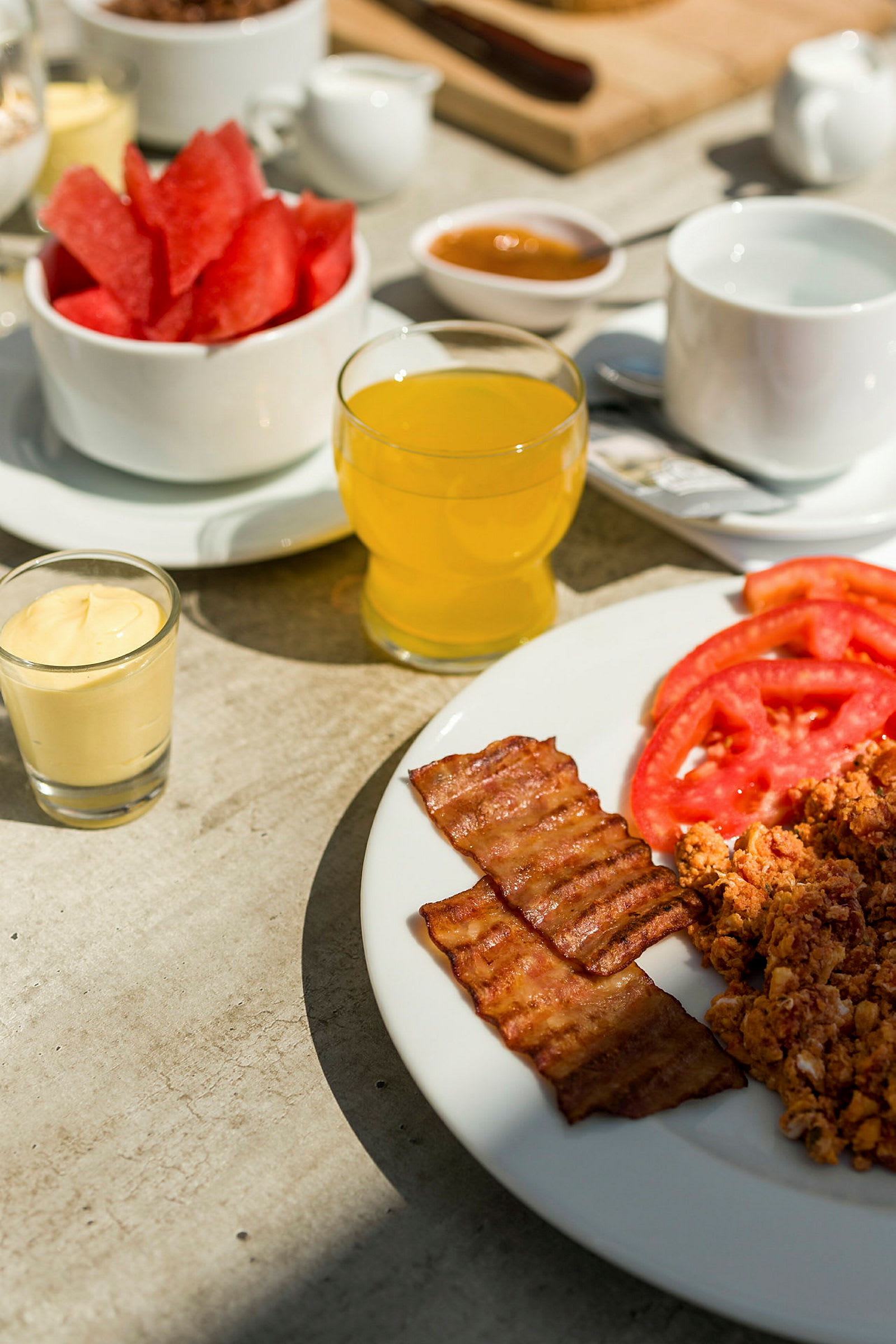 En frukost med bacon, skivade tomater, äggröra och olika drycker. (AI-genererad text)