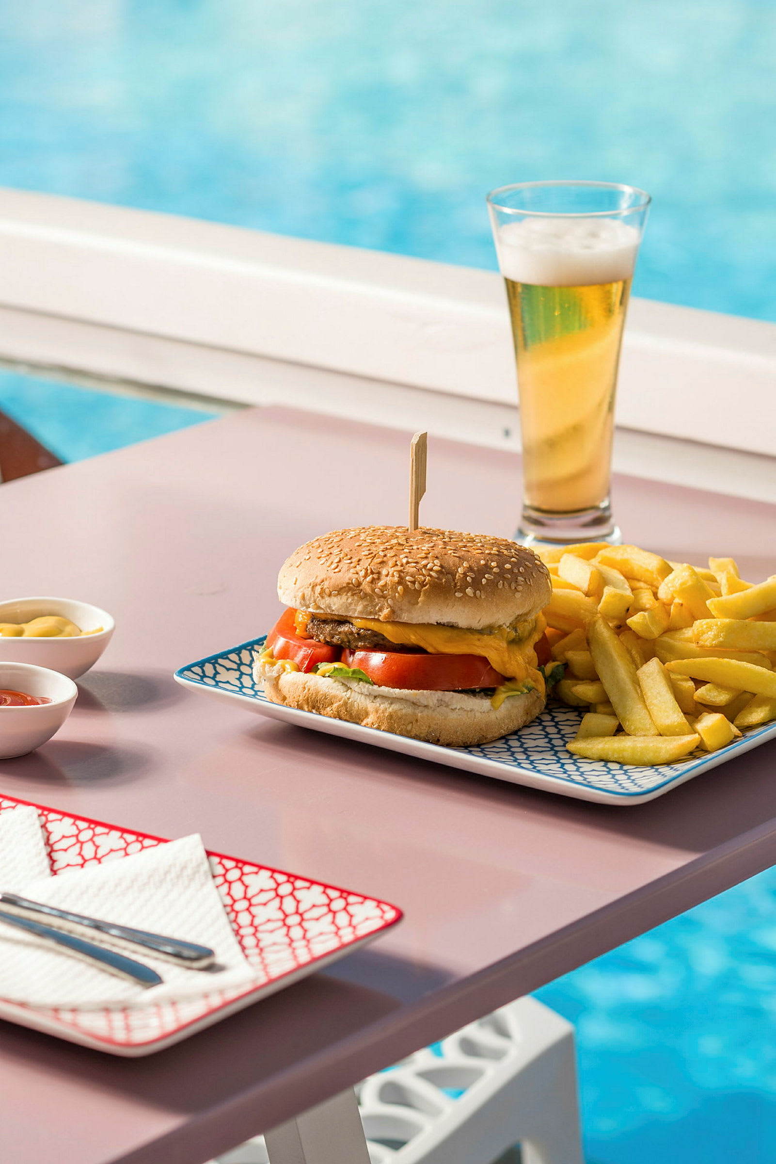 En hamburgertallrik med pommes frites och en öl nära en pool. (AI-genererad text)