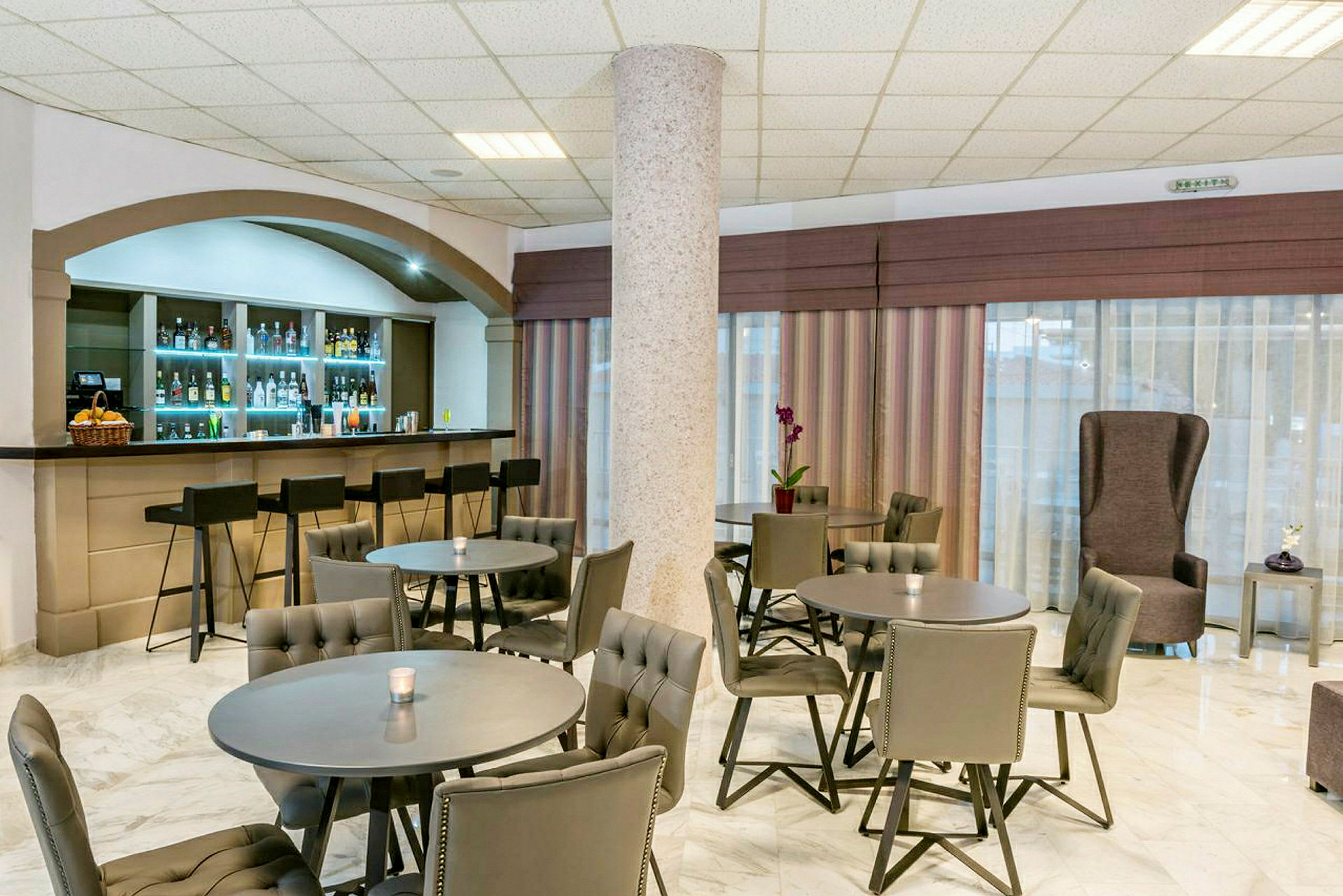 Bild på en hotellbar med flera bord och stolar, samt en bardisk med barstolar. (AI-genererad text)