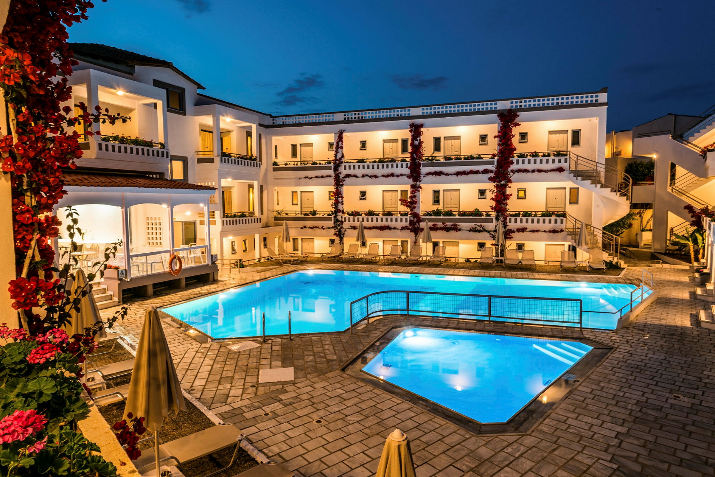 Bild på en upplyst hotellpool och byggnad under kvällstid. (AI-genererad text)
