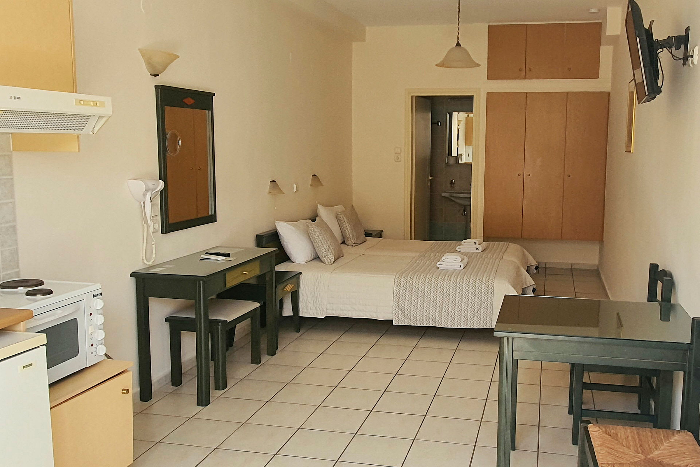 Bild av ett hotellrum med säng, bord, stolar och köksutrustning. (AI-genererad text)