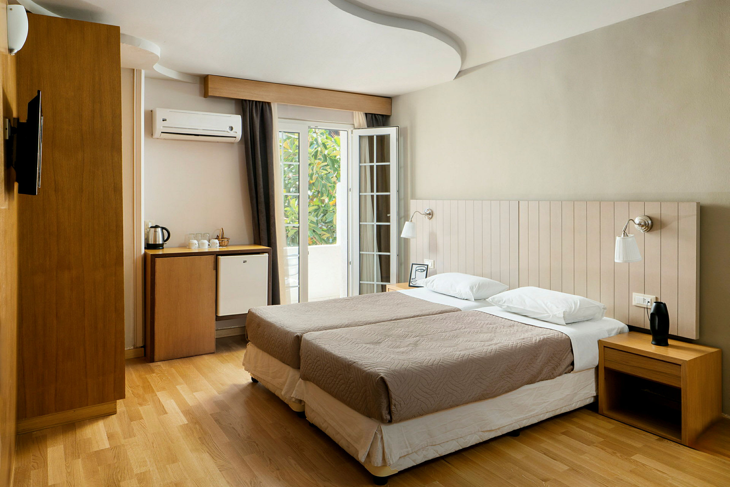 Ett hotellrum med två enkelsängar, skrivbord, minibarkyl och fransk balkong. (AI-genererad text)