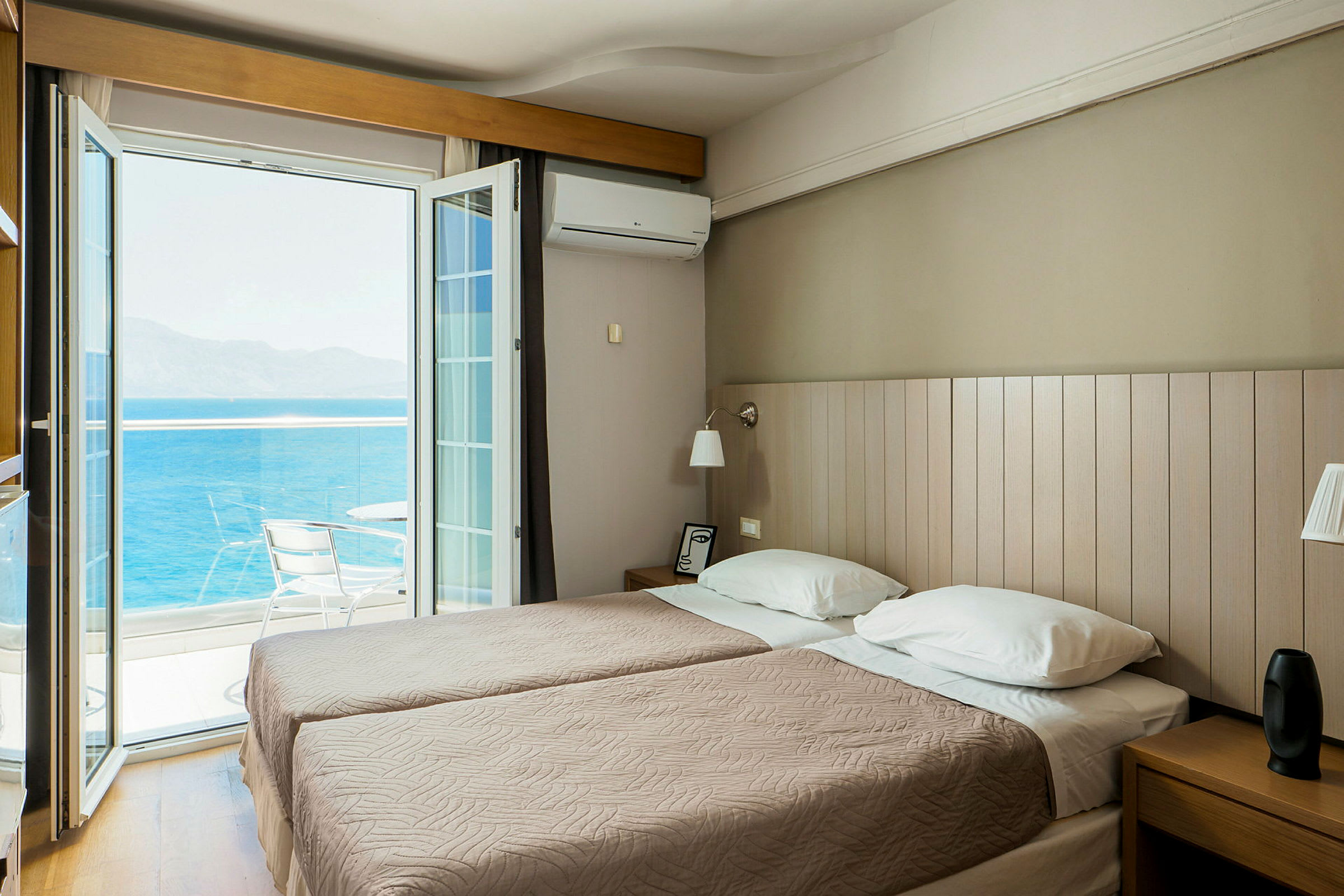 Ett hotellrum med två enkelsängar och en öppen balkongdörr som vetter mot havet. (AI-genererad text)