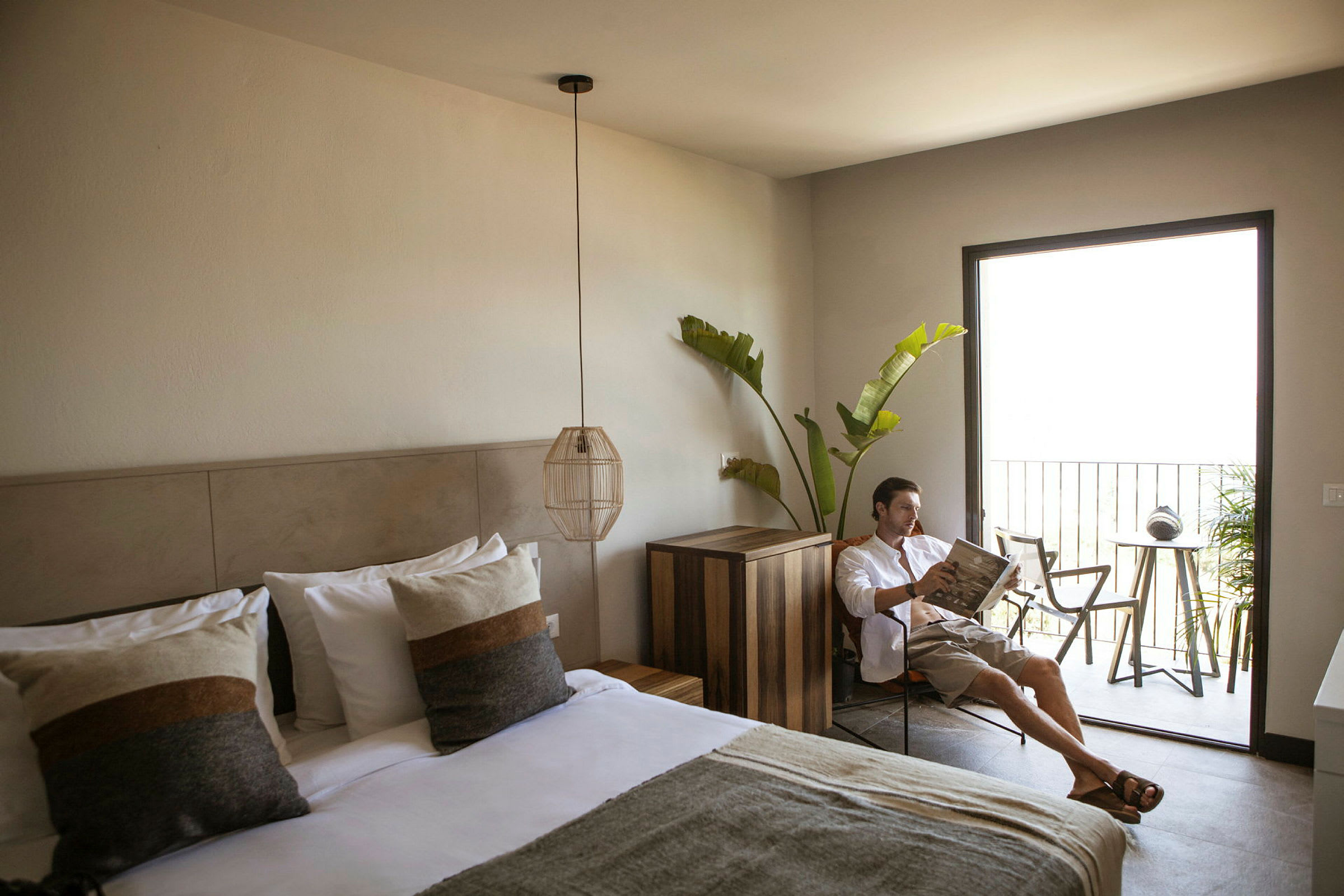 Ett hotellrum med en bäddad dubbelsäng, modern inredning, och en balkong med utemöbler samt grönska. (AI-genererad text)