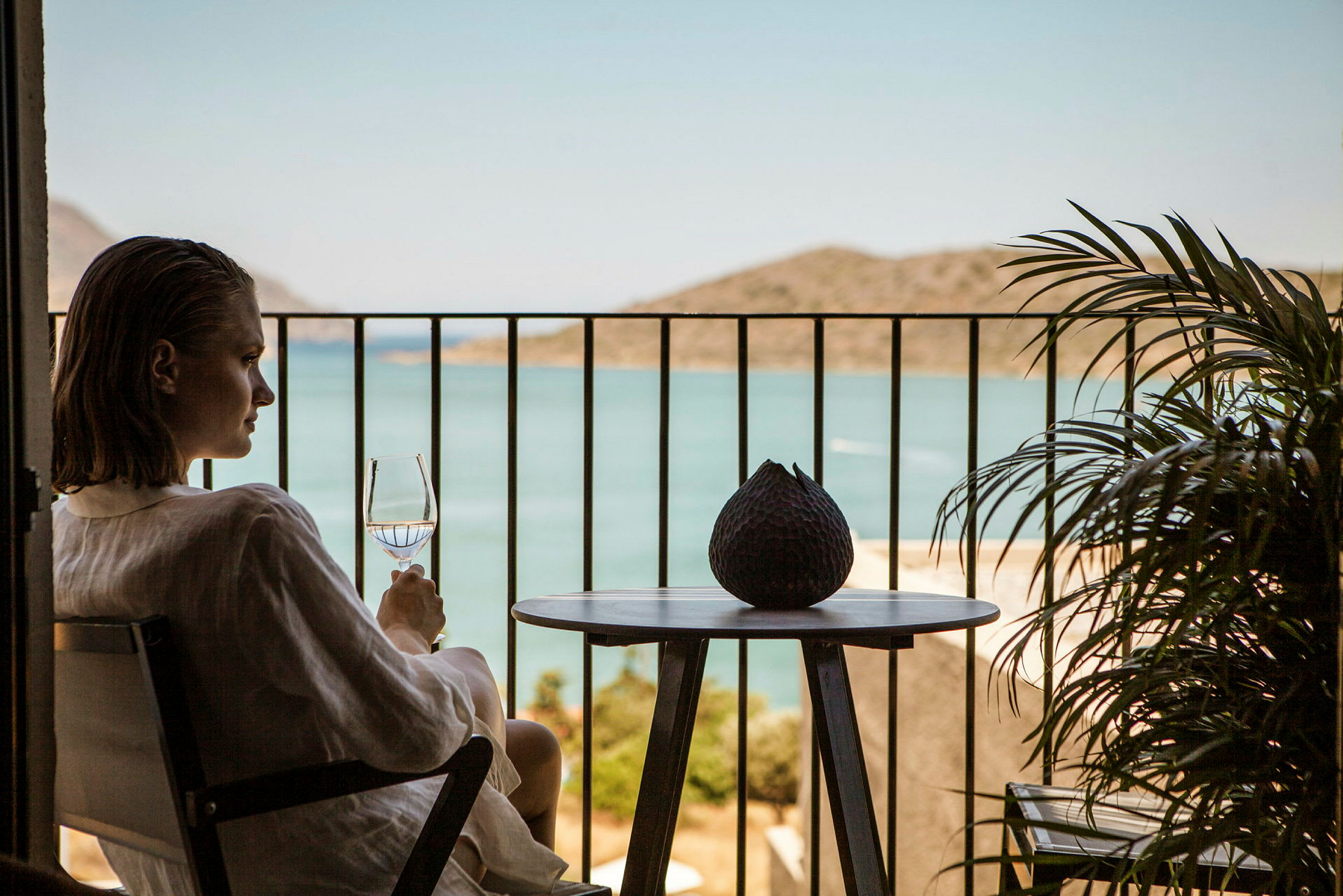 En person sitter på en balkong och håller ett glas med utsikt över havet. (AI-genererad text)