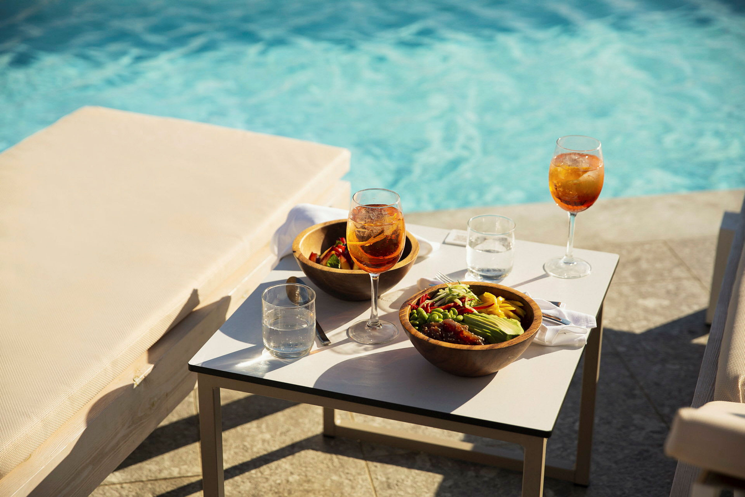 Två salladsskålar och glas med dryck på ett bord bredvid en pool. (AI-genererad text)