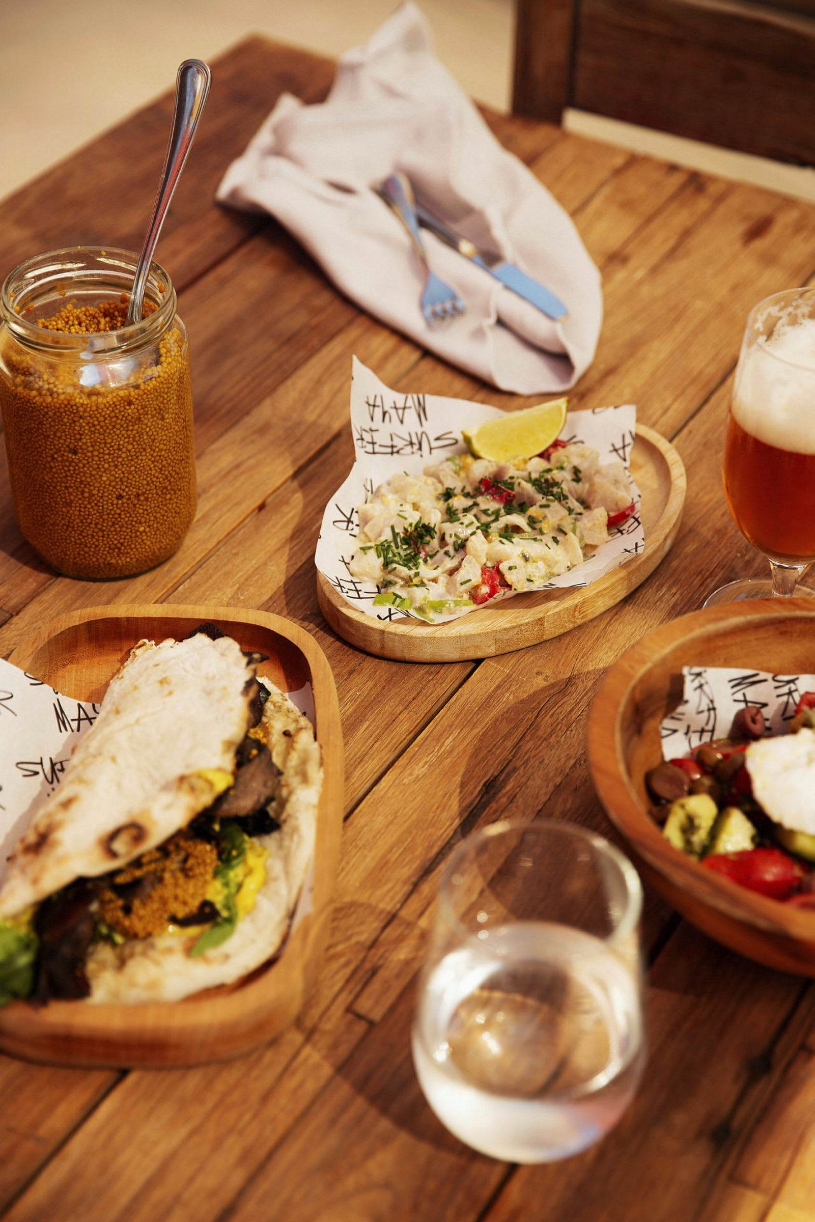 Ett bord med olika maträtter, inklusive en wrap, en sallad och en öl. (AI-genererad text)