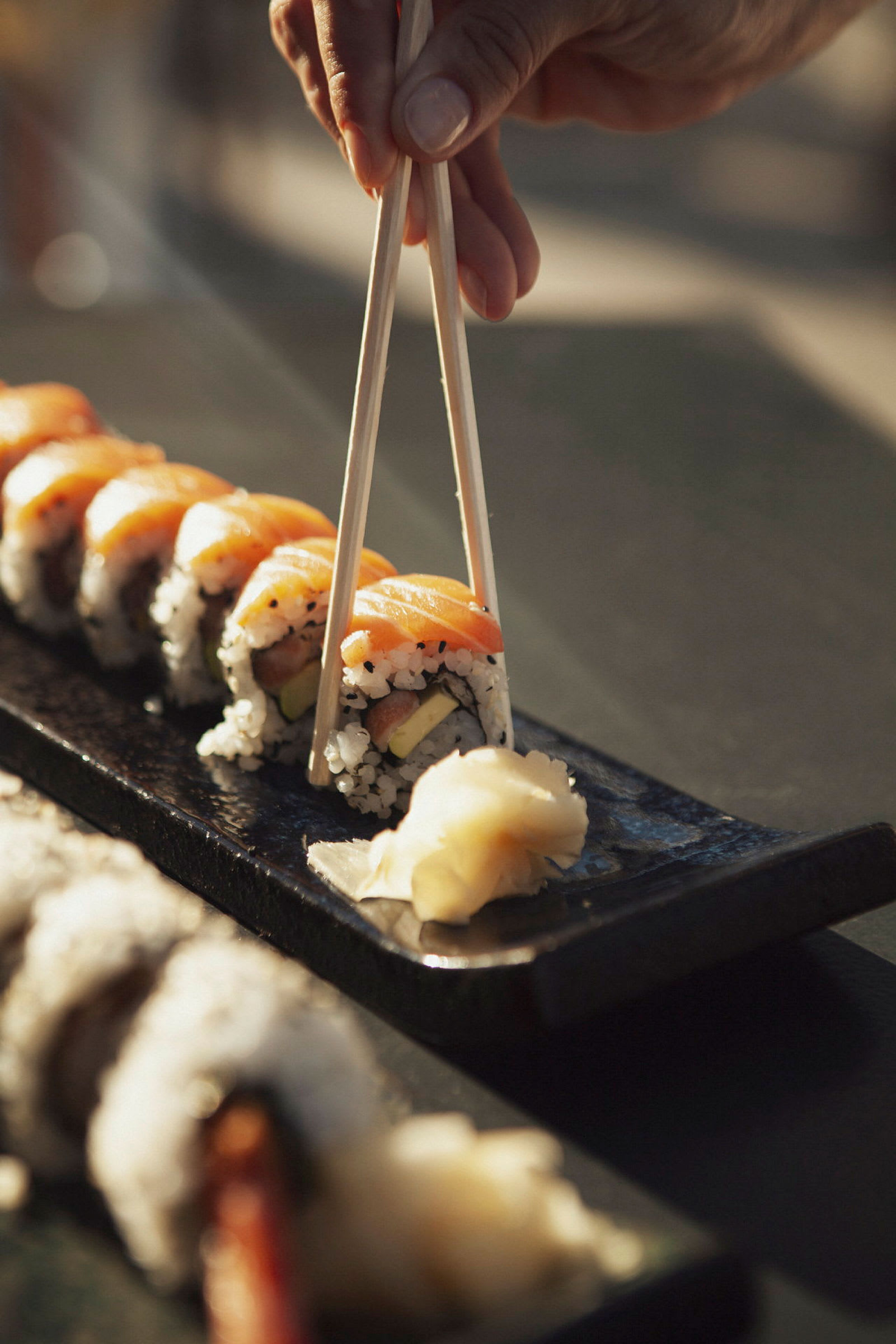 Hand håller ätpinnar och tar sushi från ett fat. (AI-genererad text)