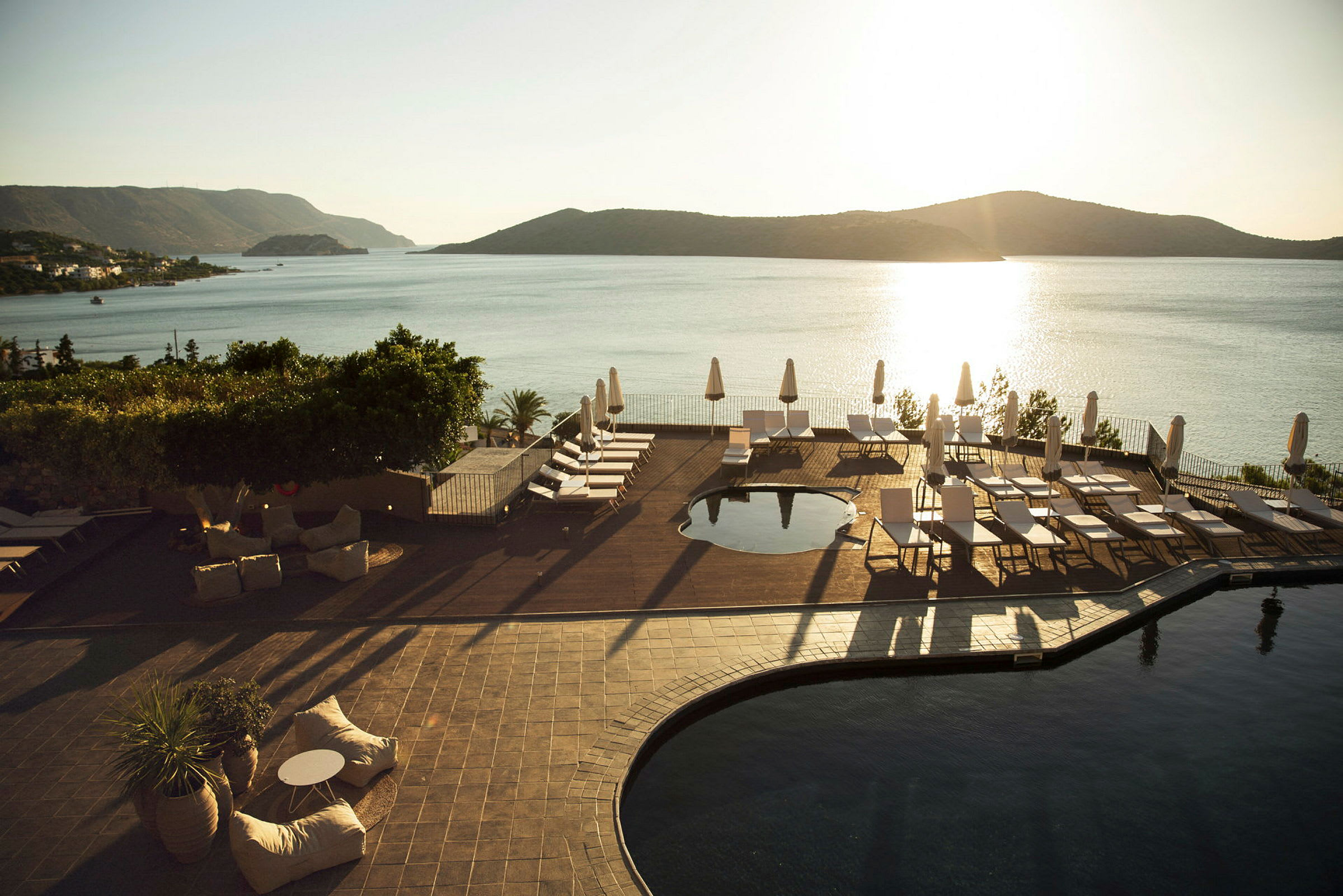 En hotellpoolområde med solstolar och parasoller nära havet med en solnedgång. (AI-genererad text)