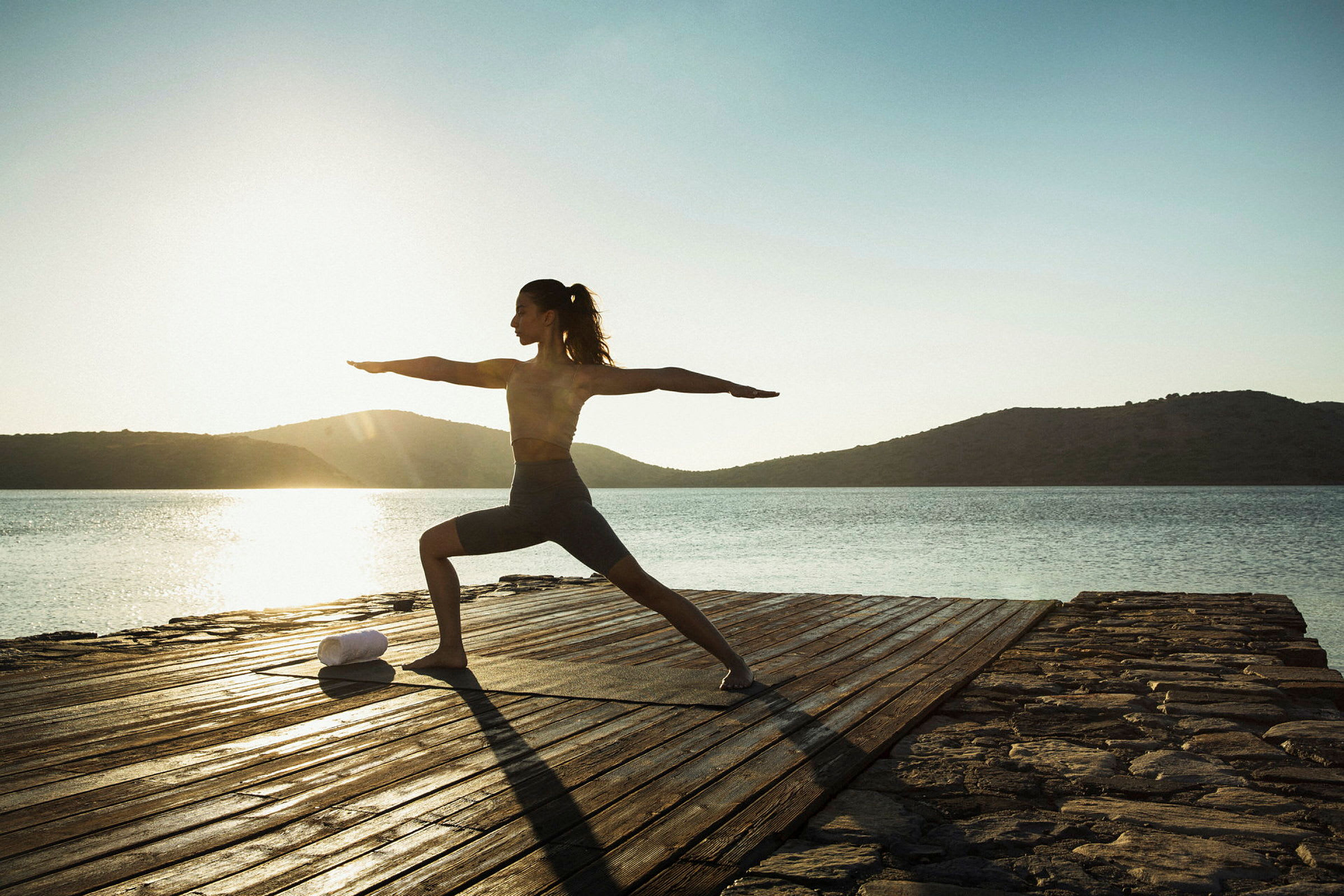 Person som utför yogaposition på en träplattform nära vatten i soluppgång. (AI-genererad text)
