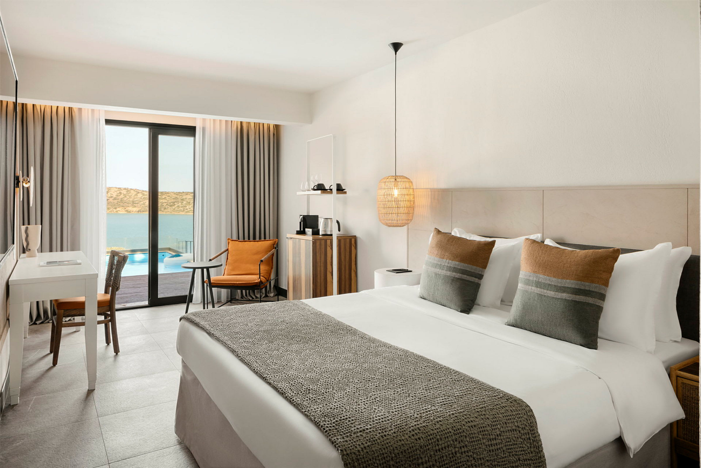 Hotellrum med dubbelsäng, skrivbord och sittgrupp, med utsikt över pool och hav. (AI-genererad text)
