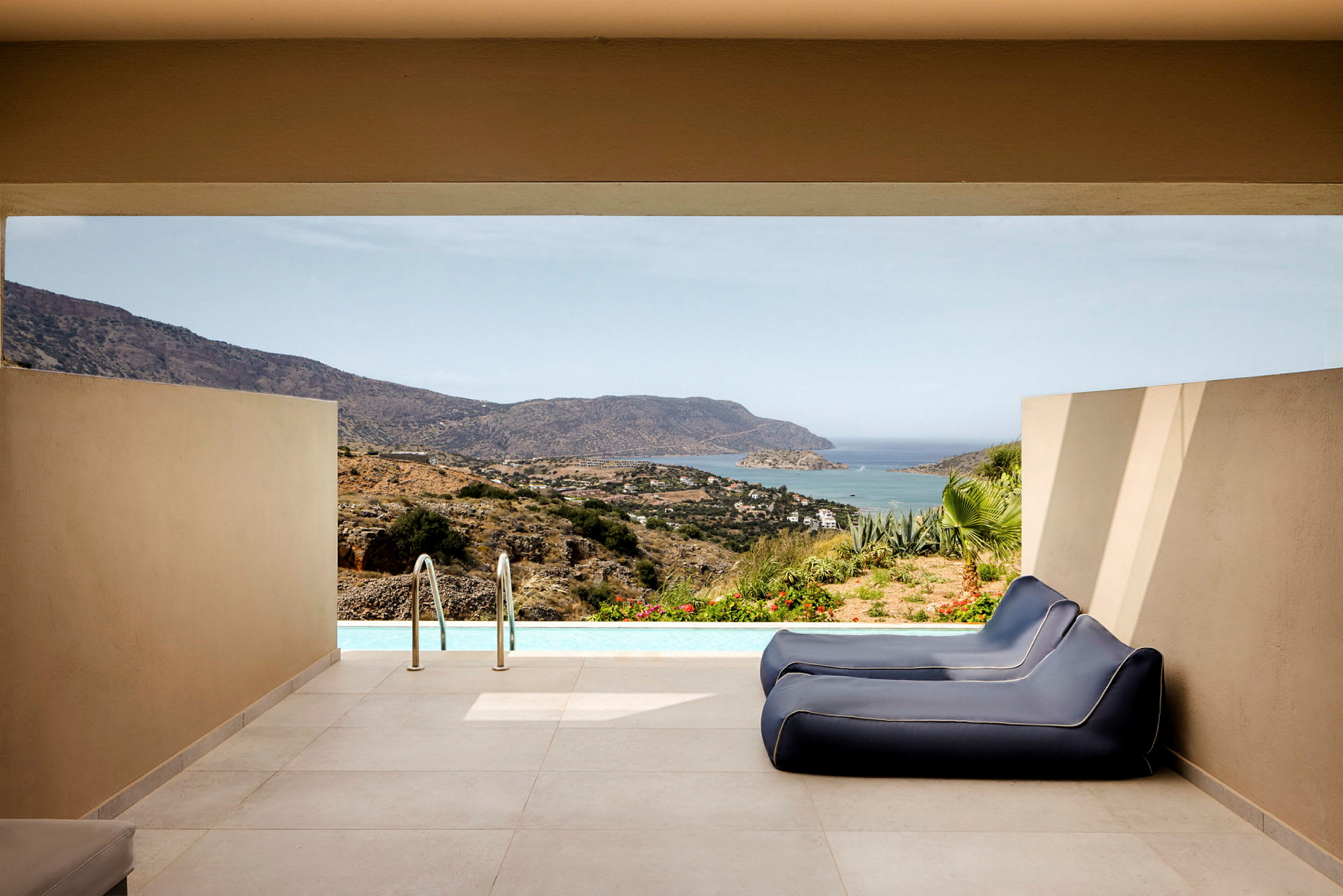 Privat pool med två blå solstolar och utsikt över havet och bergigt landskap. (AI-genererad text)