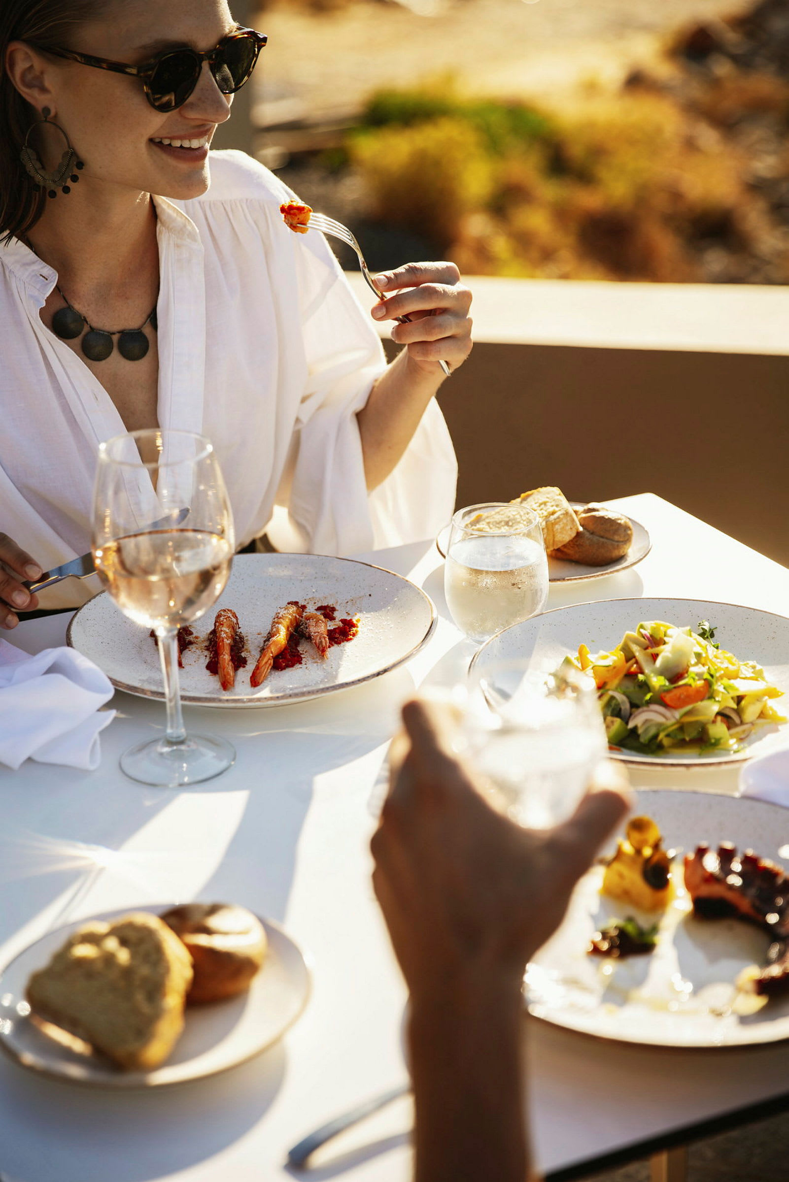 Person som sitter vid ett bord med måltid och glas vin utomhus. (AI-genererad text)