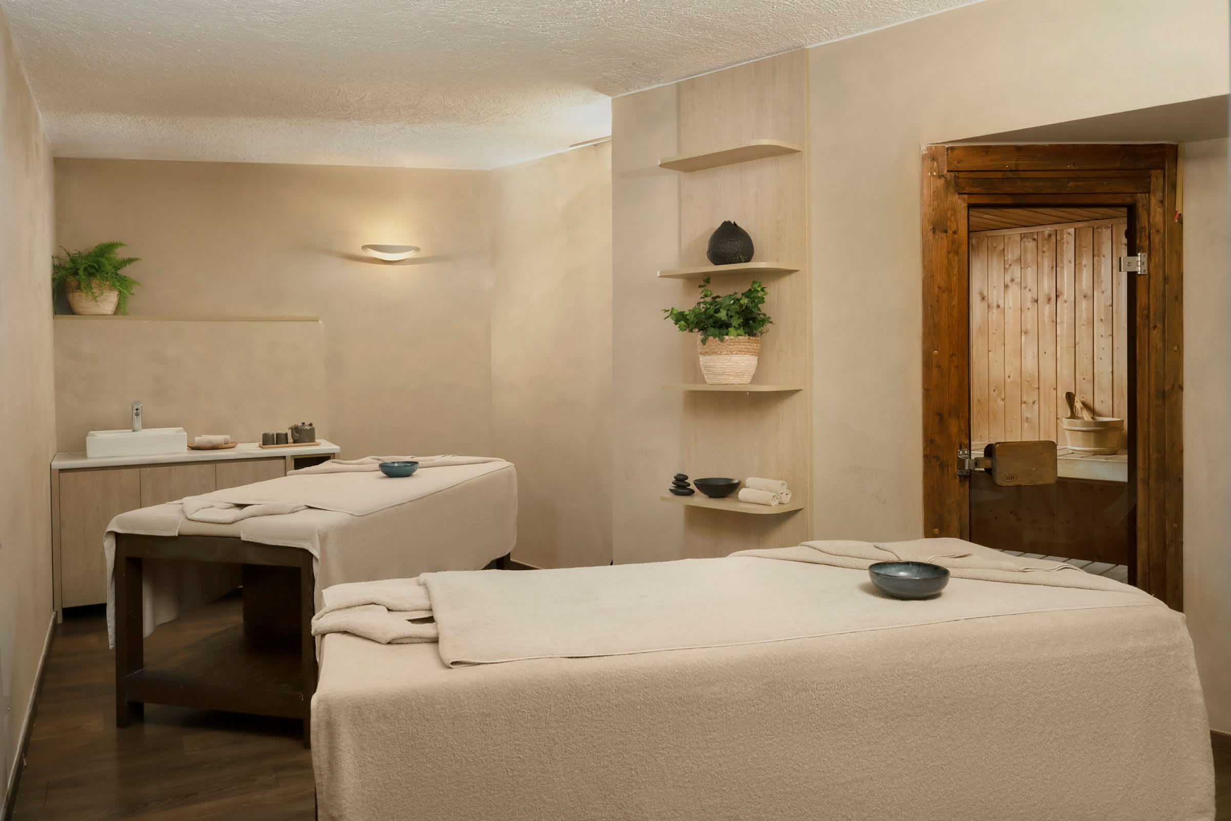 Två massagebänkar i ett spa-rum med neutrala färger, dekorativa föremål och växter. (AI-genererad text)