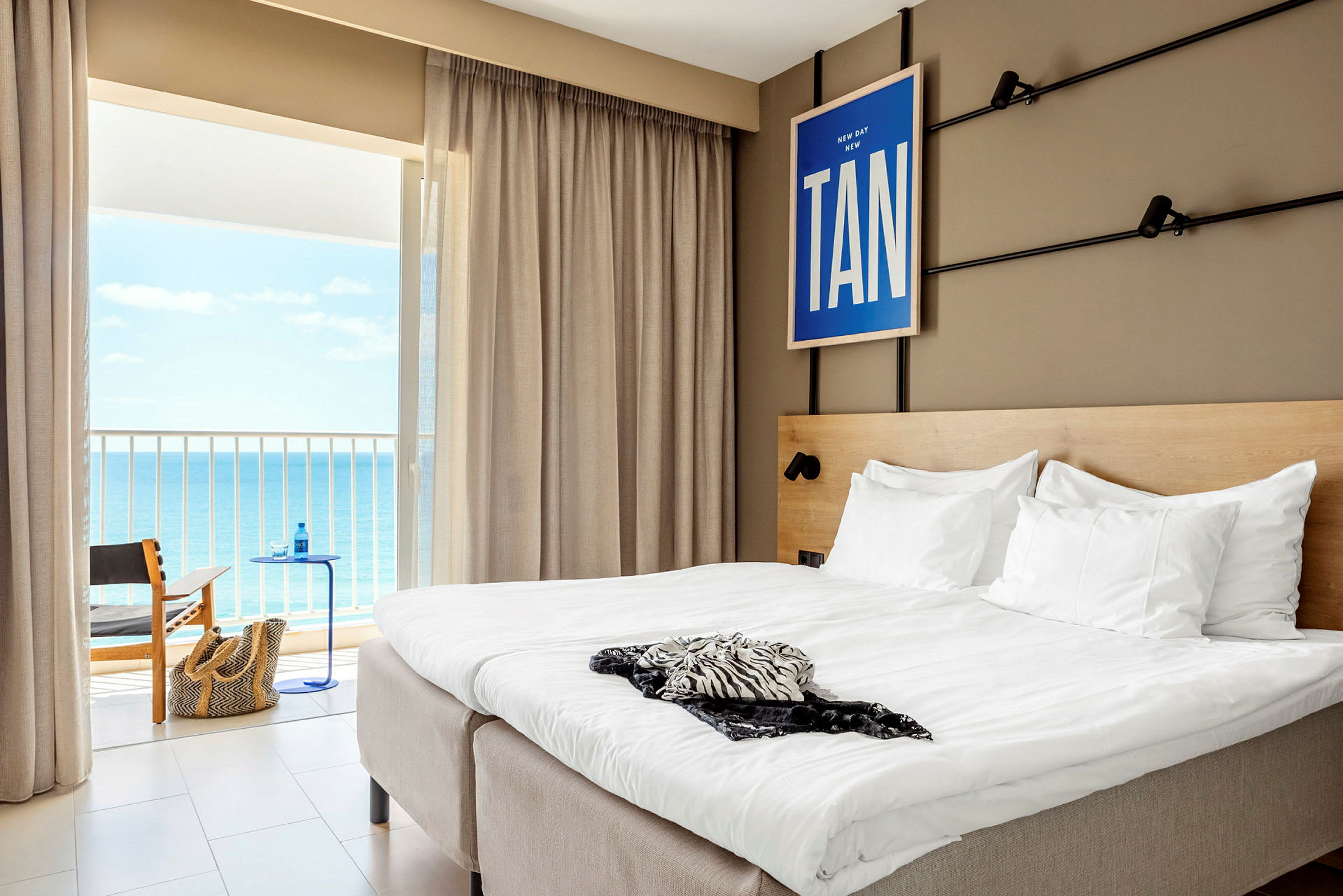 Hotellrum med en dubbelsäng och utsikt mot havet genom balkongdörren. (AI-genererad text)