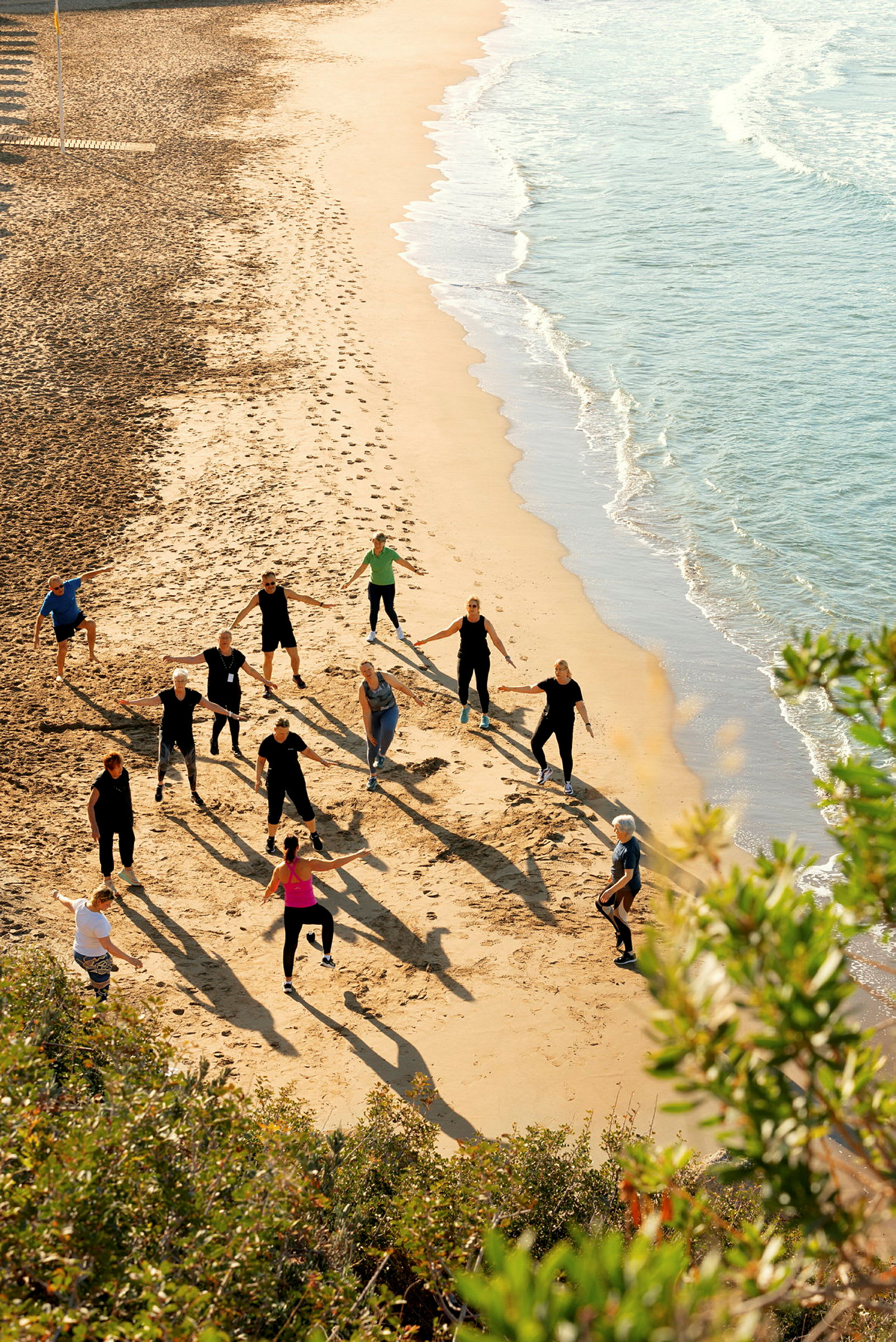 En grupp människor utför träningsaktiviteter på en sandstrand nära havet. (AI-genererad text)
