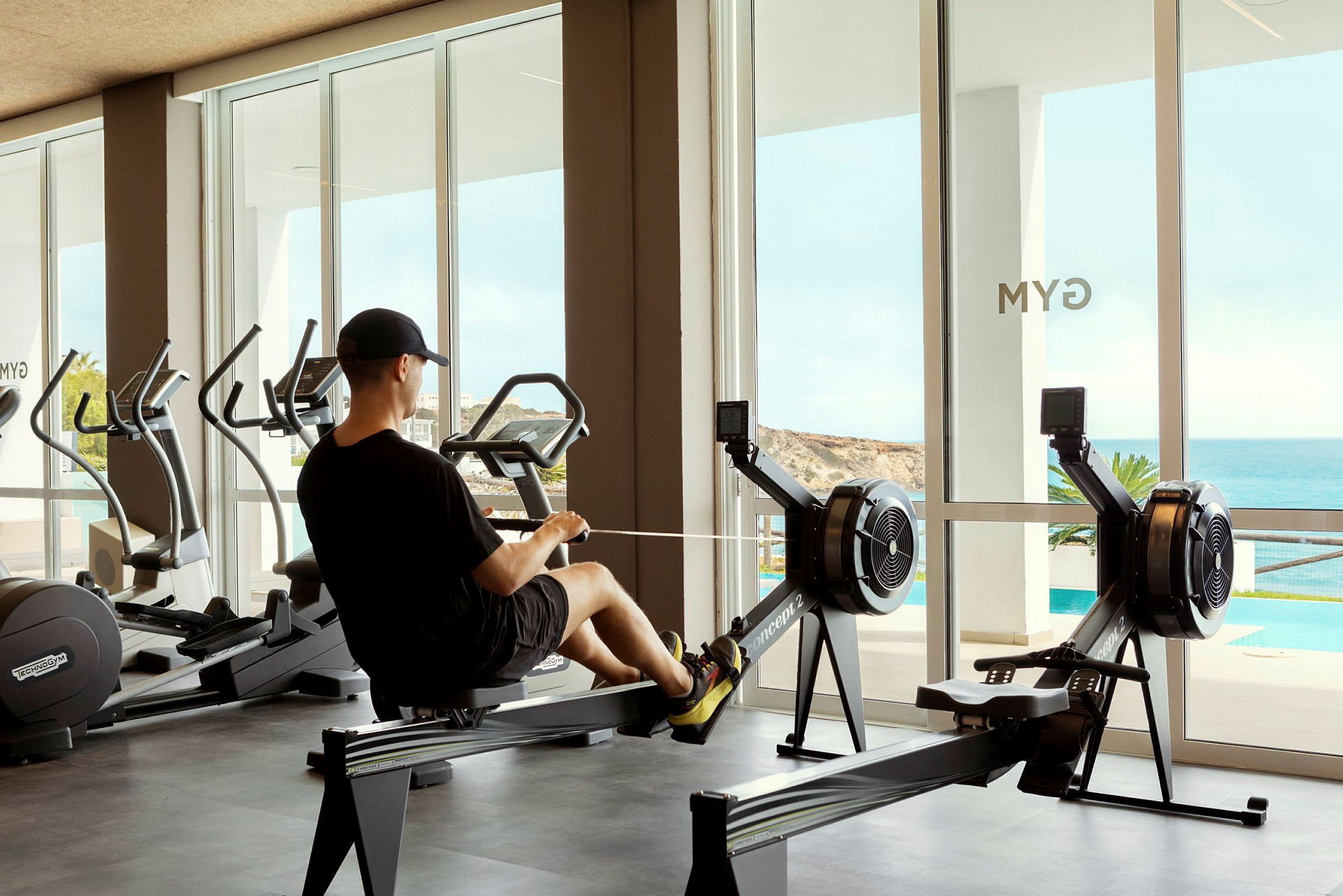 En person tränar på en roddmaskin i ett gym med stora fönster. (AI-genererad text)