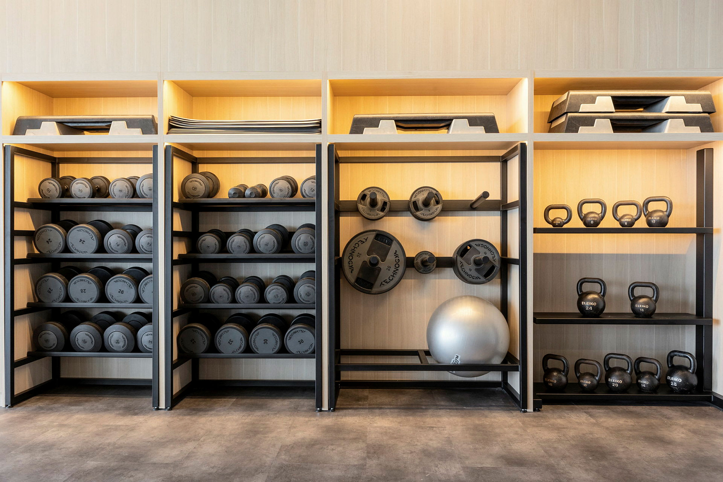 Hylla med hantlar, viktskivor, kettlebells och träningsutrustning. (AI-genererad text)