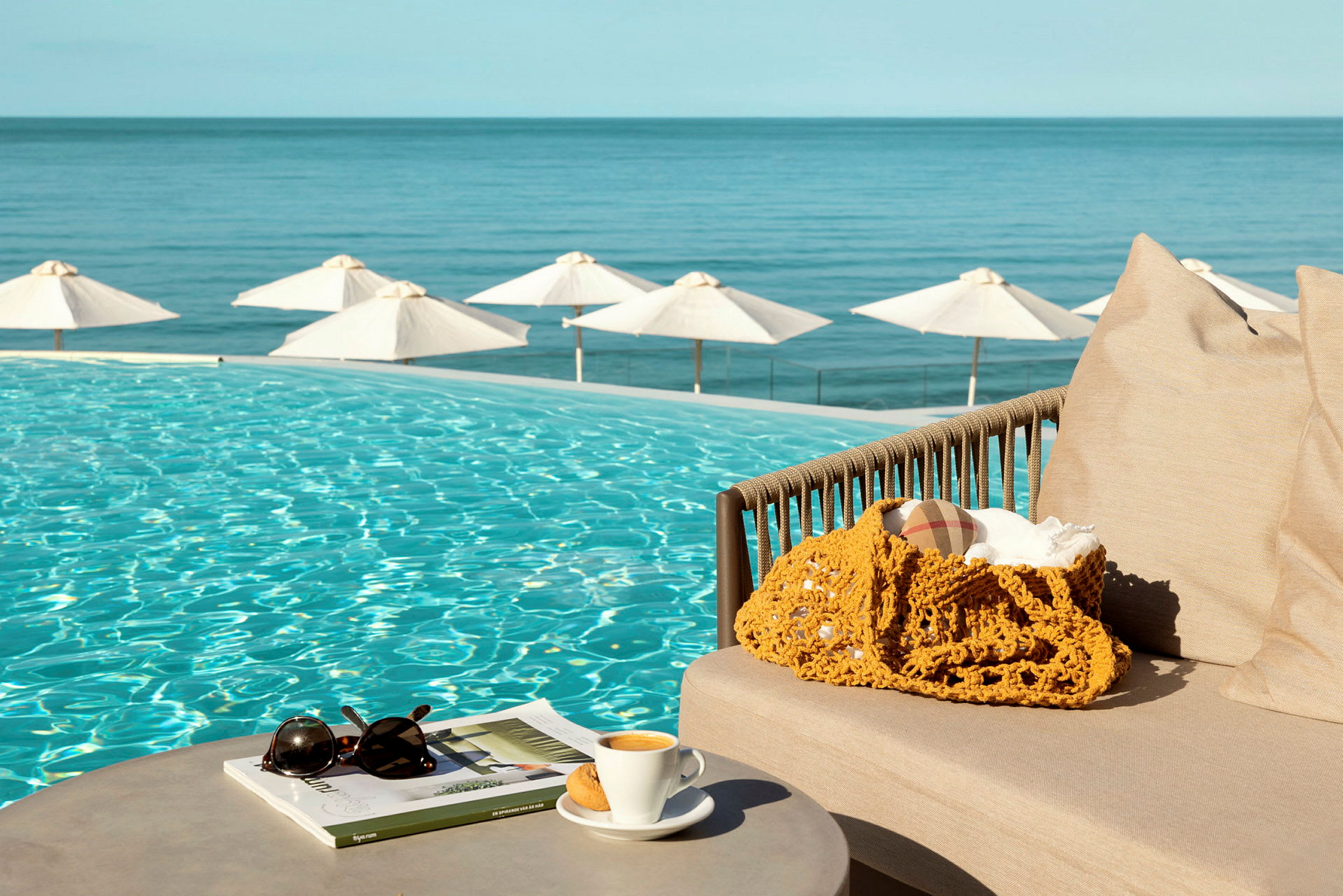 Soffa nära en pool med utsikt över havet och parasoller. (AI-genererad text)