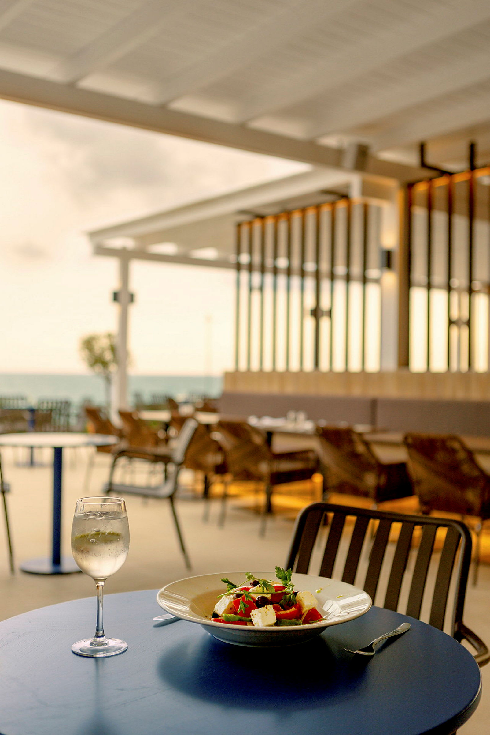 Uteservering vid havet med en tallrik sallad och ett glas vitt vin på ett bord. (AI-genererad text)