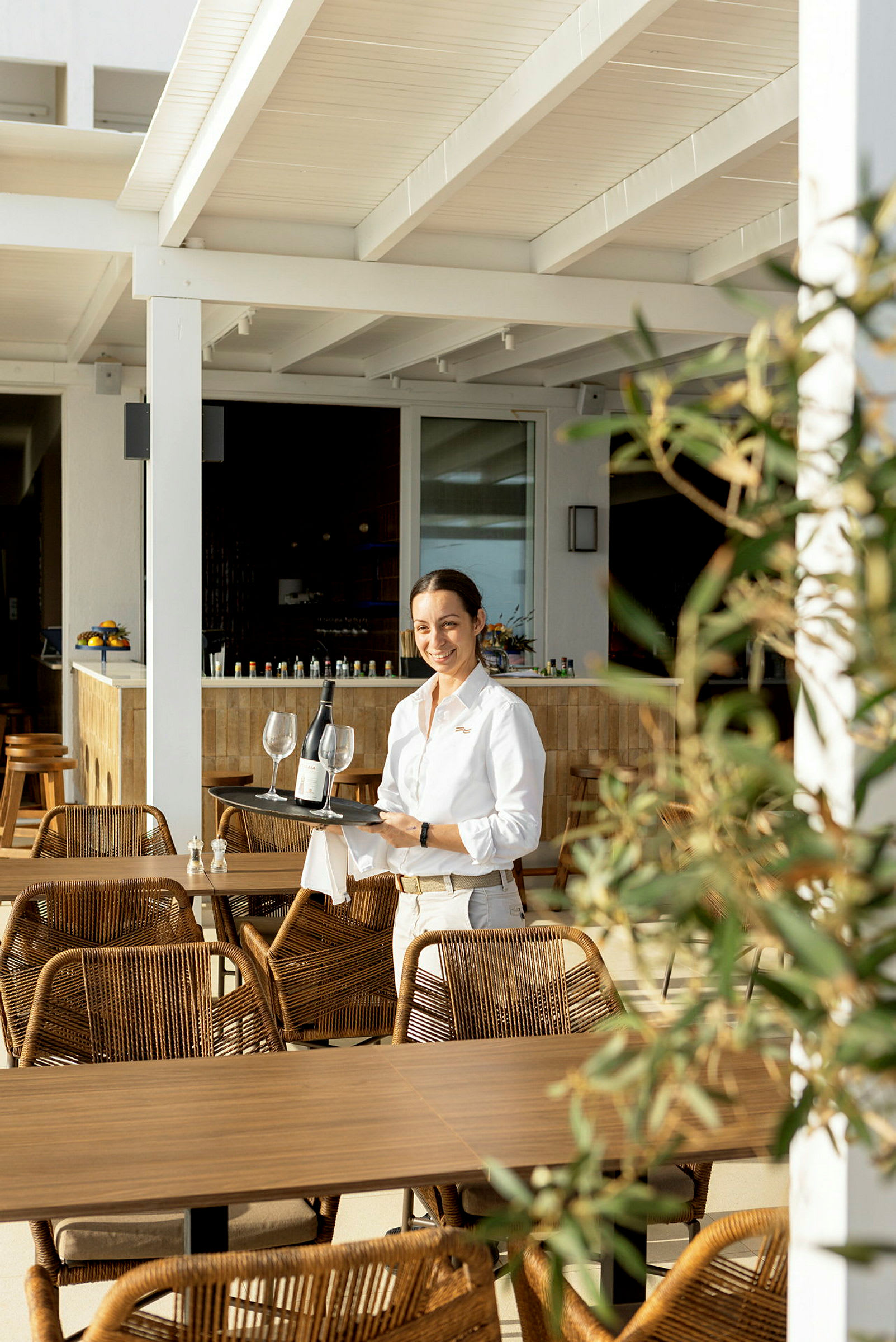 Servitör bär en bricka med vin och glas på en restaurangterrass. (AI-genererad text)
