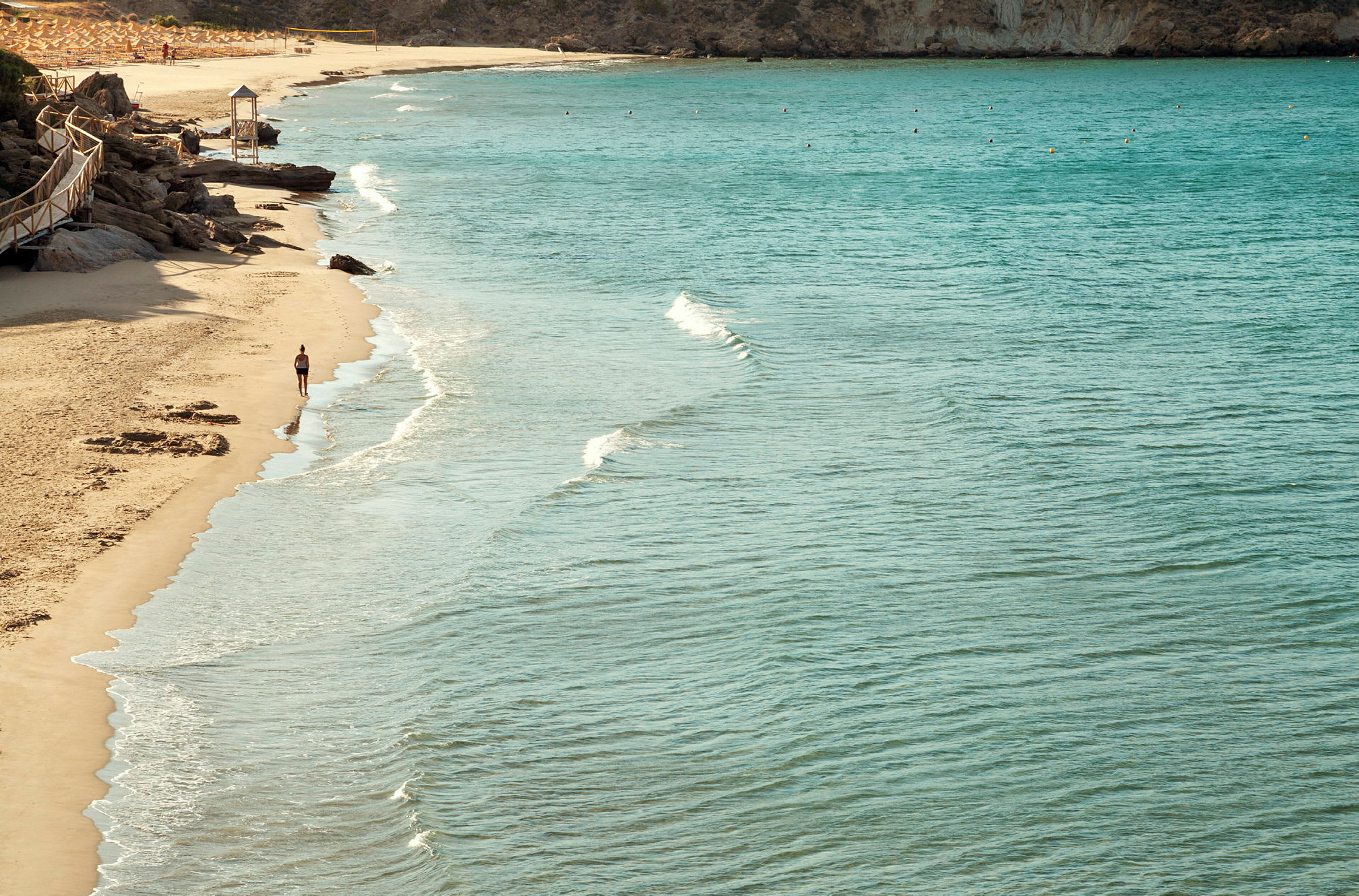 Strand med klart vatten och en person som går längs strandkanten. (AI-genererad text)