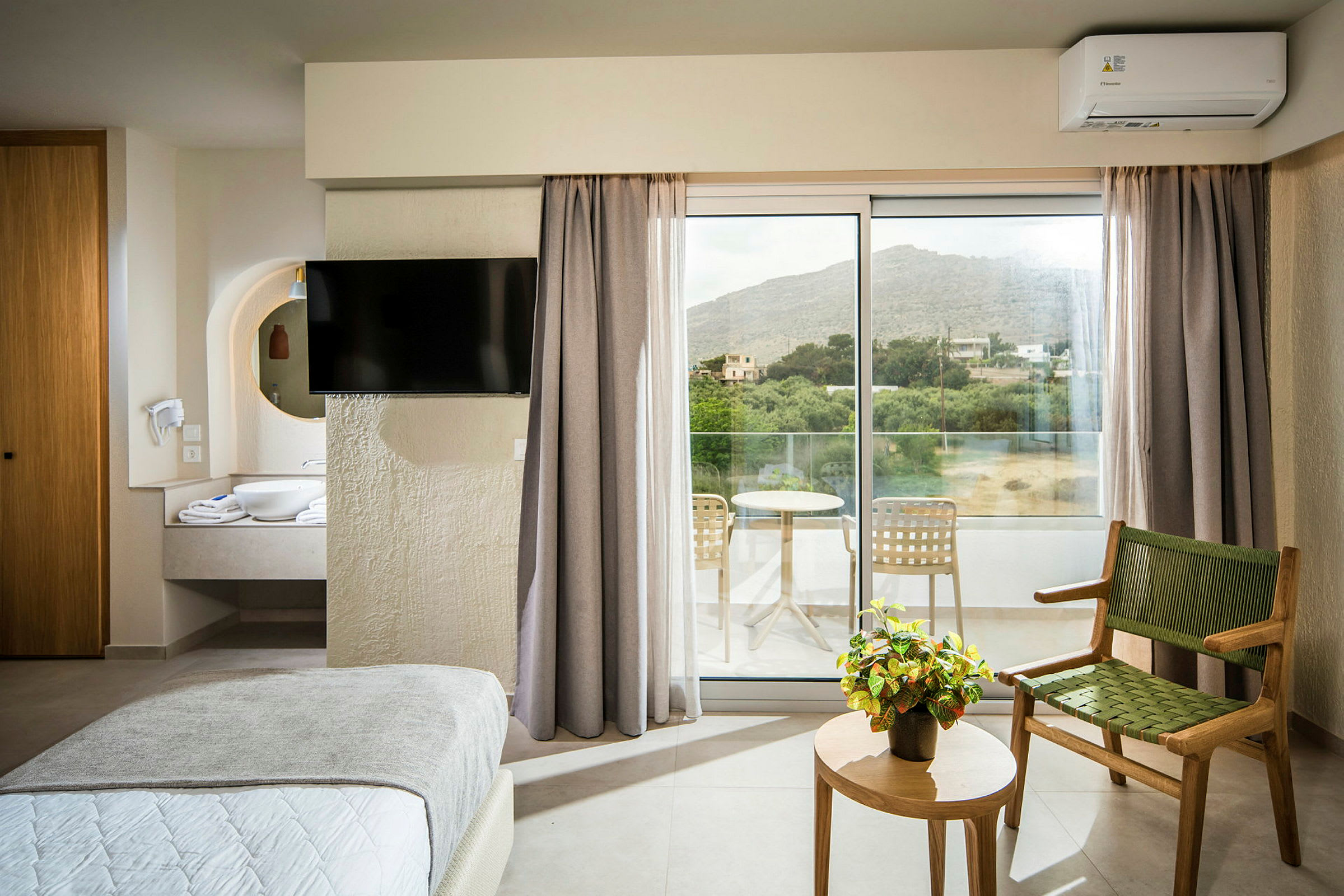 Hotellrum med säng, TV, stol, bord med en växt och utgång till balkong. (AI-genererad text)