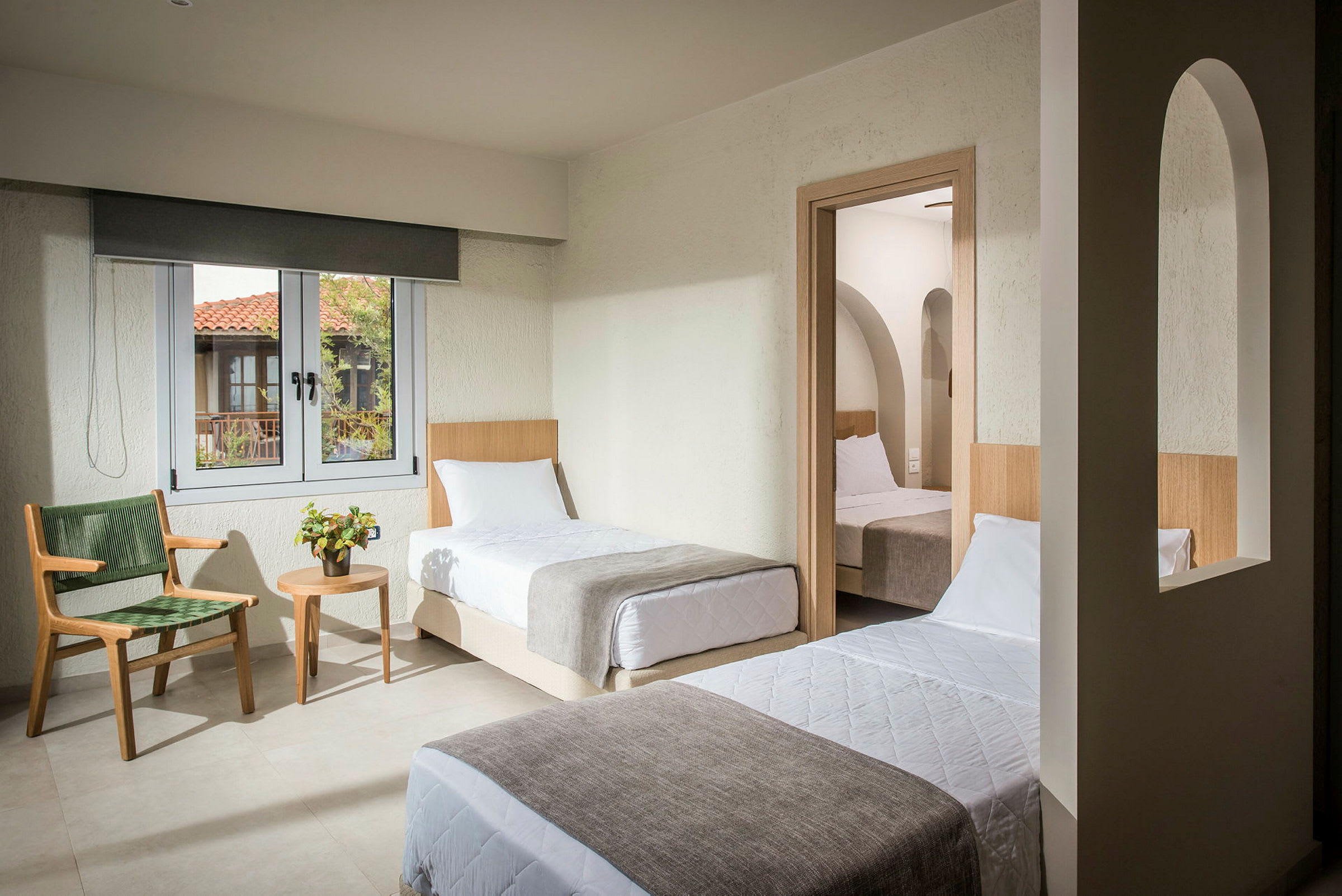 Ett hotellrum med två enkelsängar, ett fönster och en dörr till ett annat rum med en säng. (AI-genererad text)