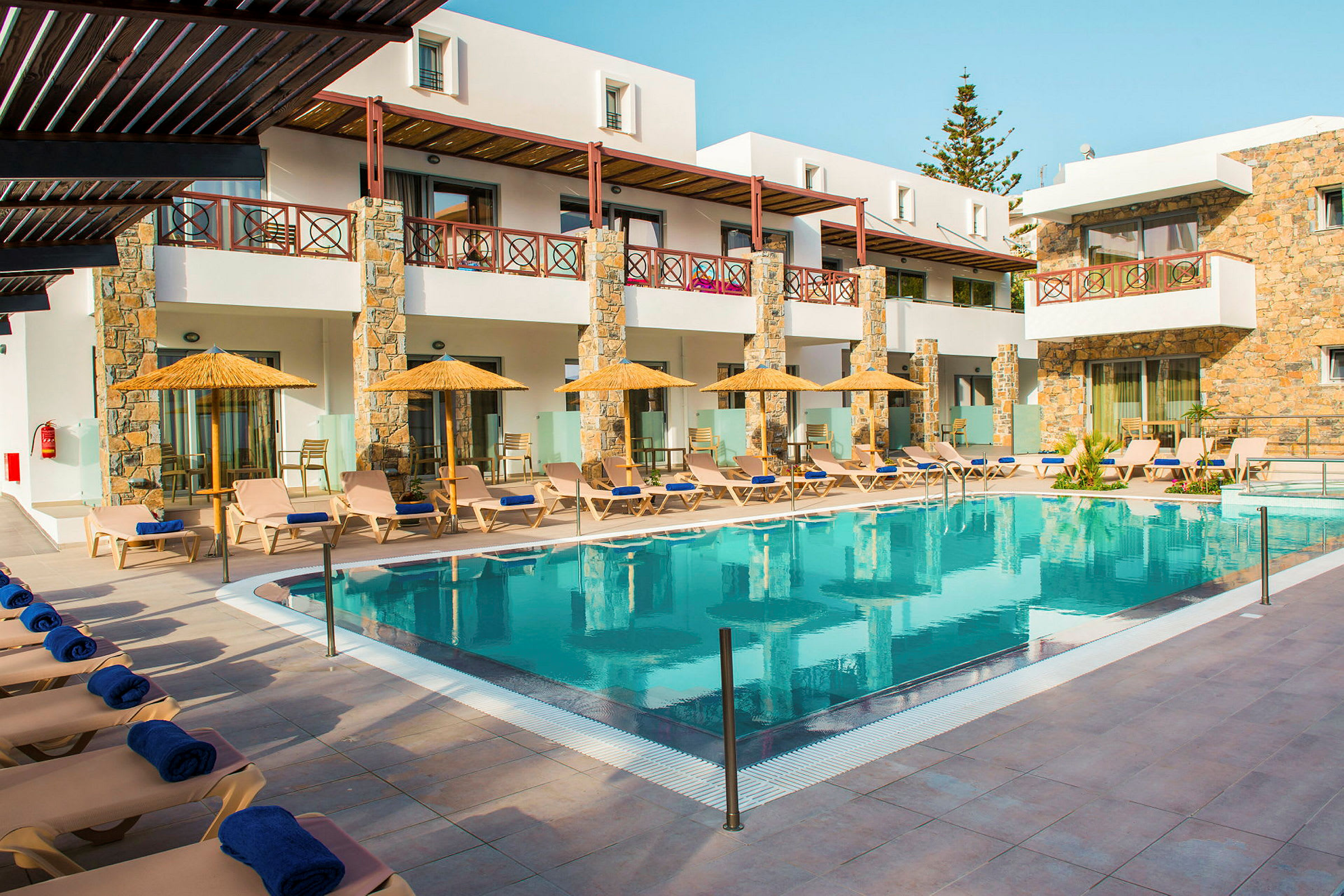 Bild av en pool med solstolar och parasoll framför en byggnad. (AI-genererad text)