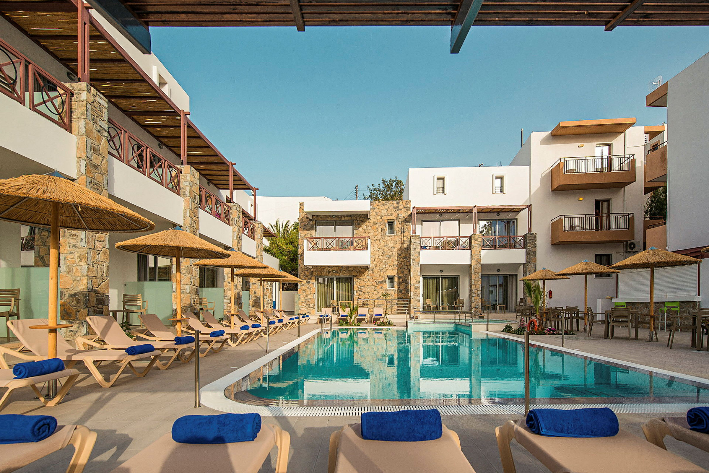 Hotellets poolområde med solstolar och parasoller framför byggnaden. (AI-genererad text)