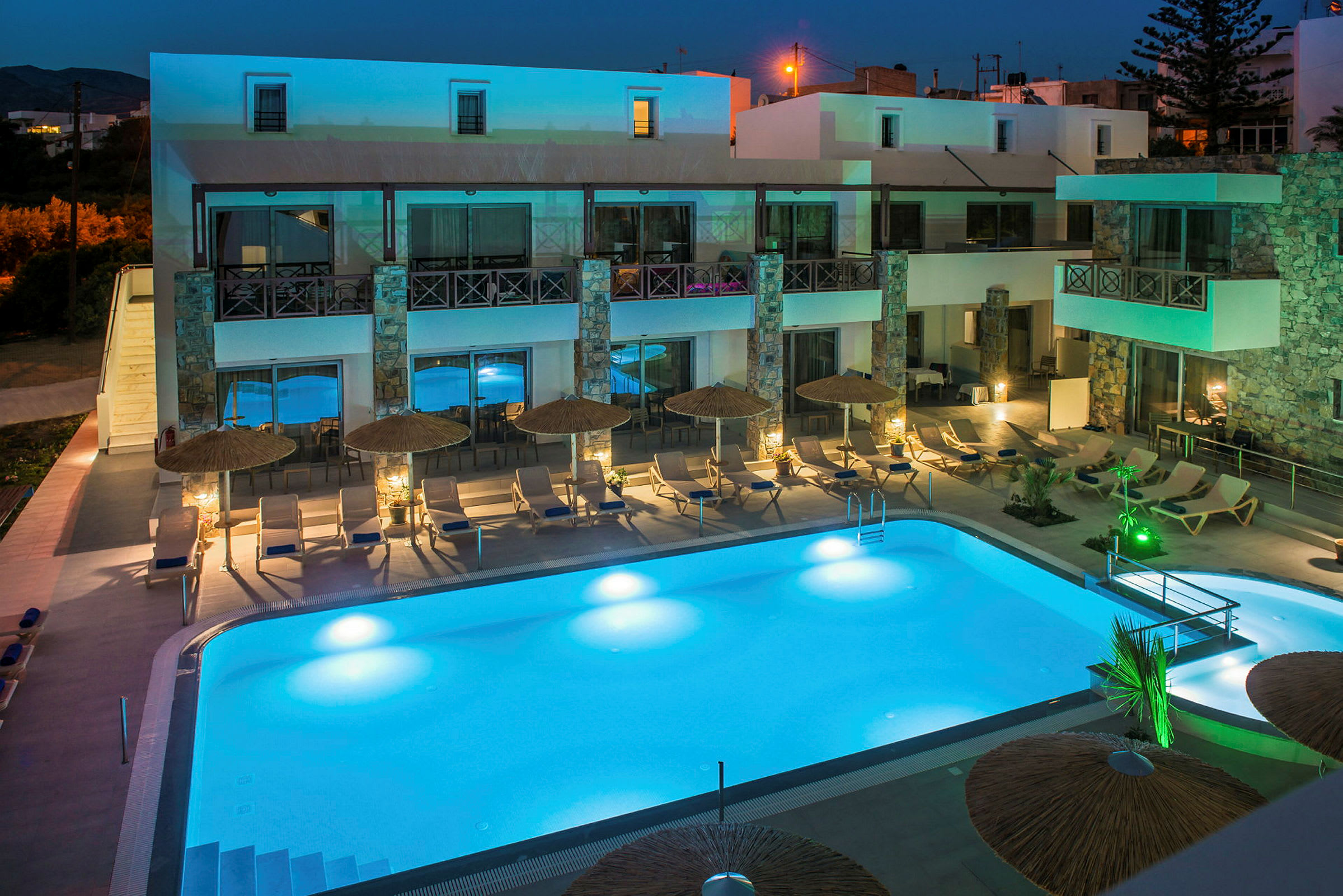 Hotellet i kvällsbelysning med upplyst poolområde och solstolar. (AI-genererad text)