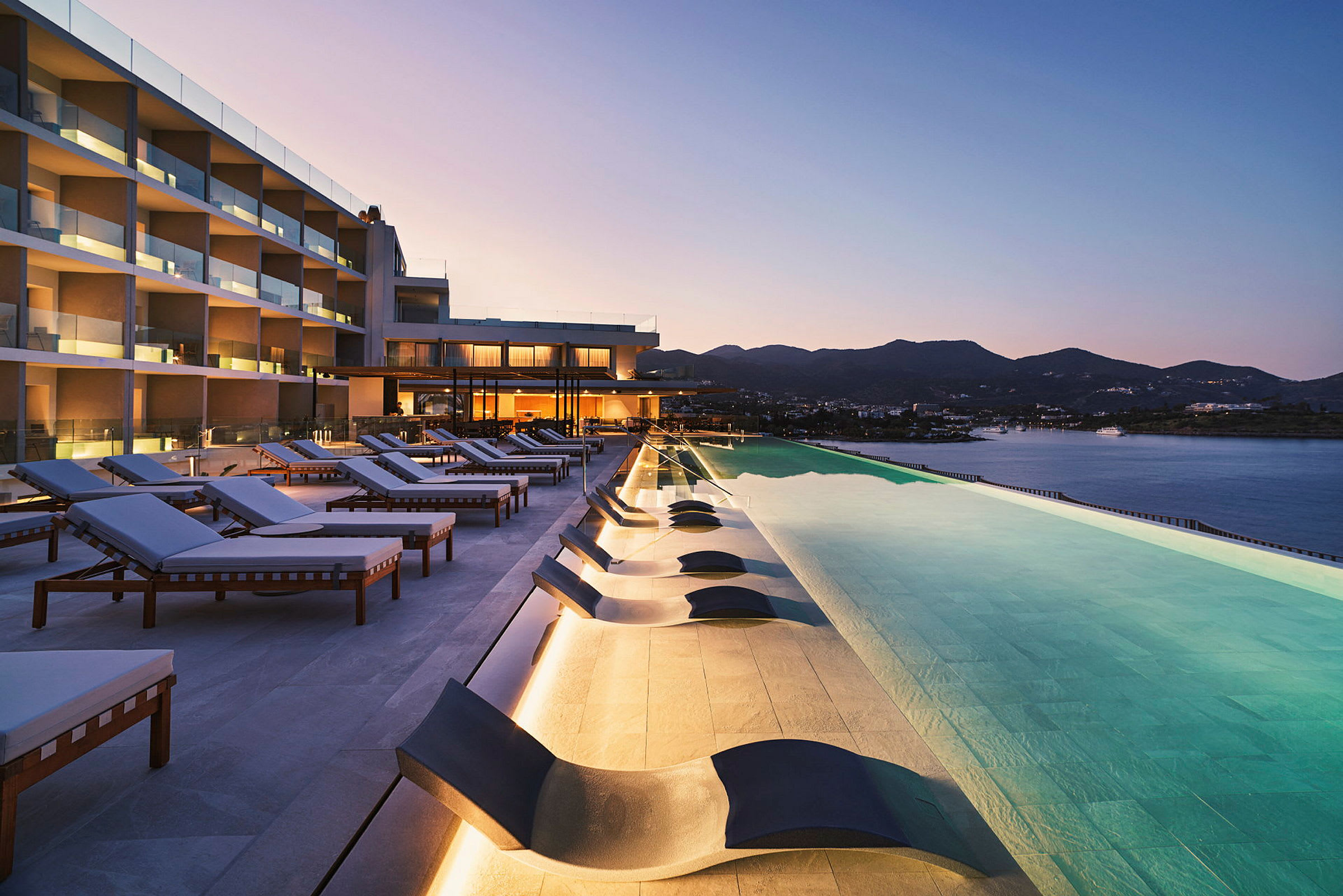 Solstolar vid en infinity-pool med utsikt över hav och berg. (AI-genererad text)