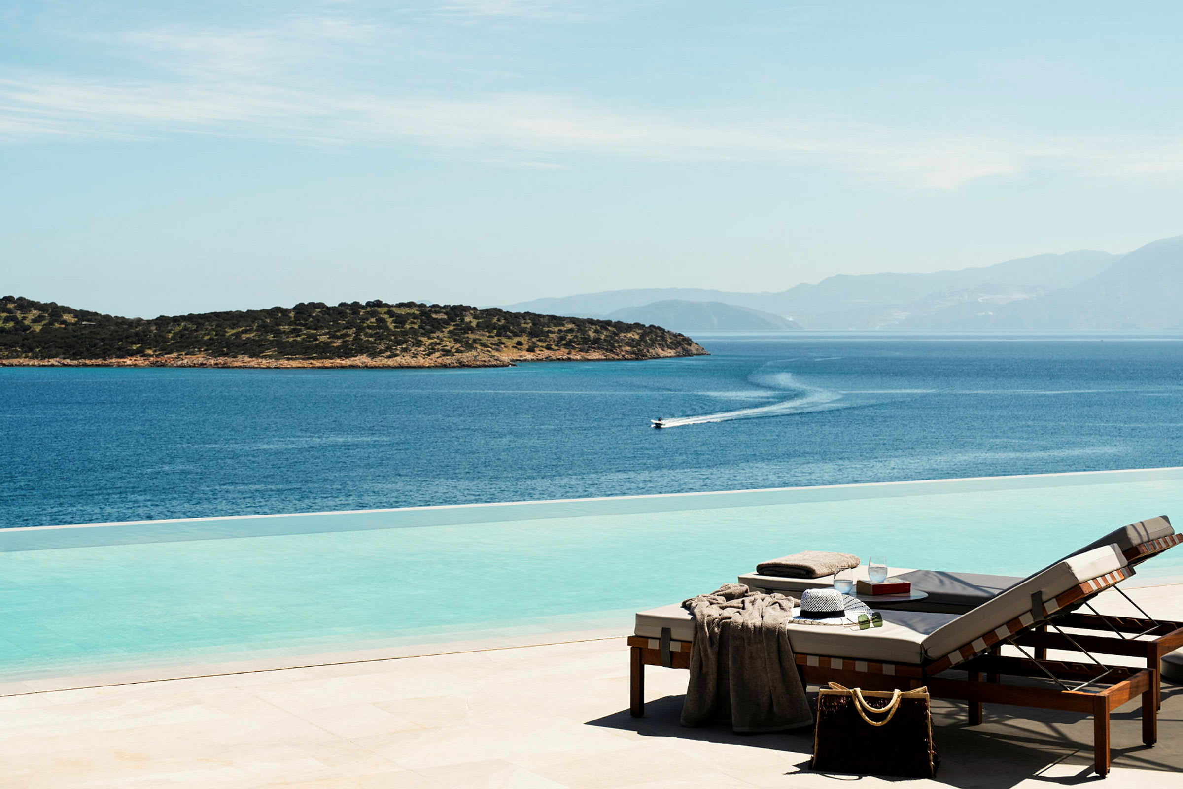 Solstolar vid en infinitypool med utsikt över havet och en liten ö. (AI-genererad text)