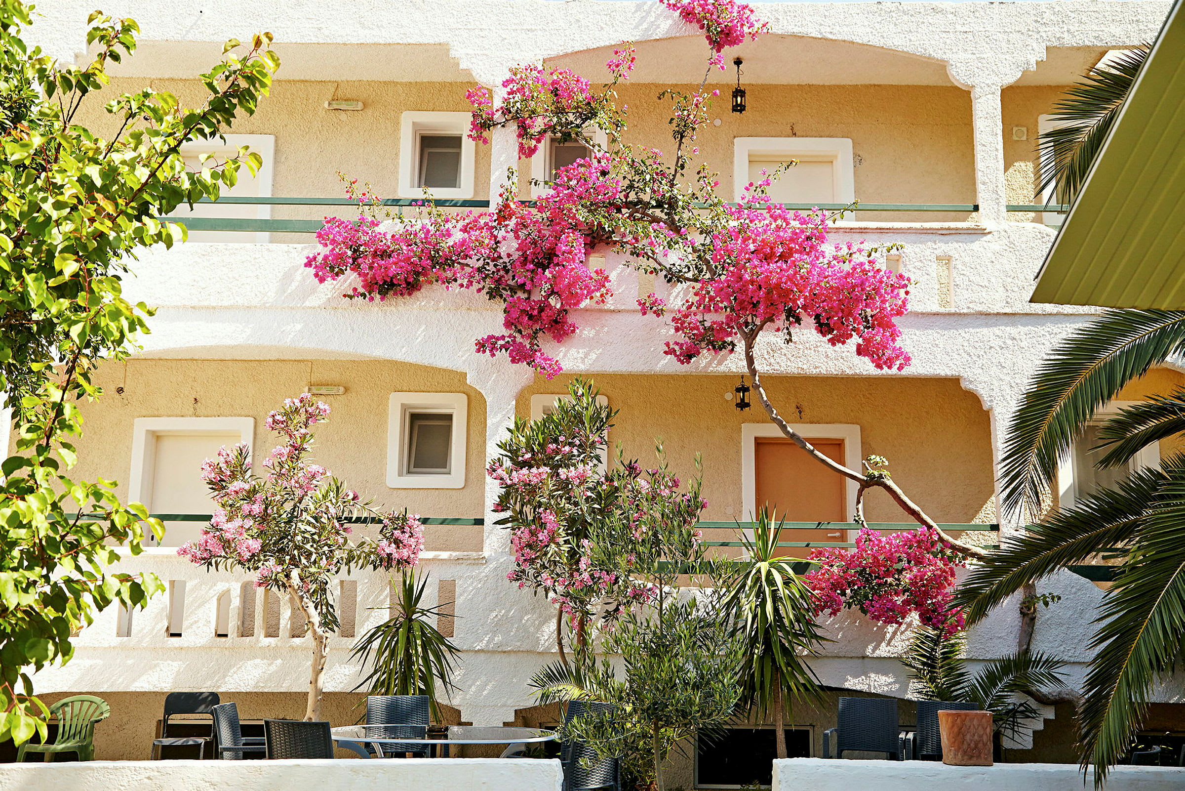 Vit byggnad med rosa blommor och grönska. (AI-genererad text)