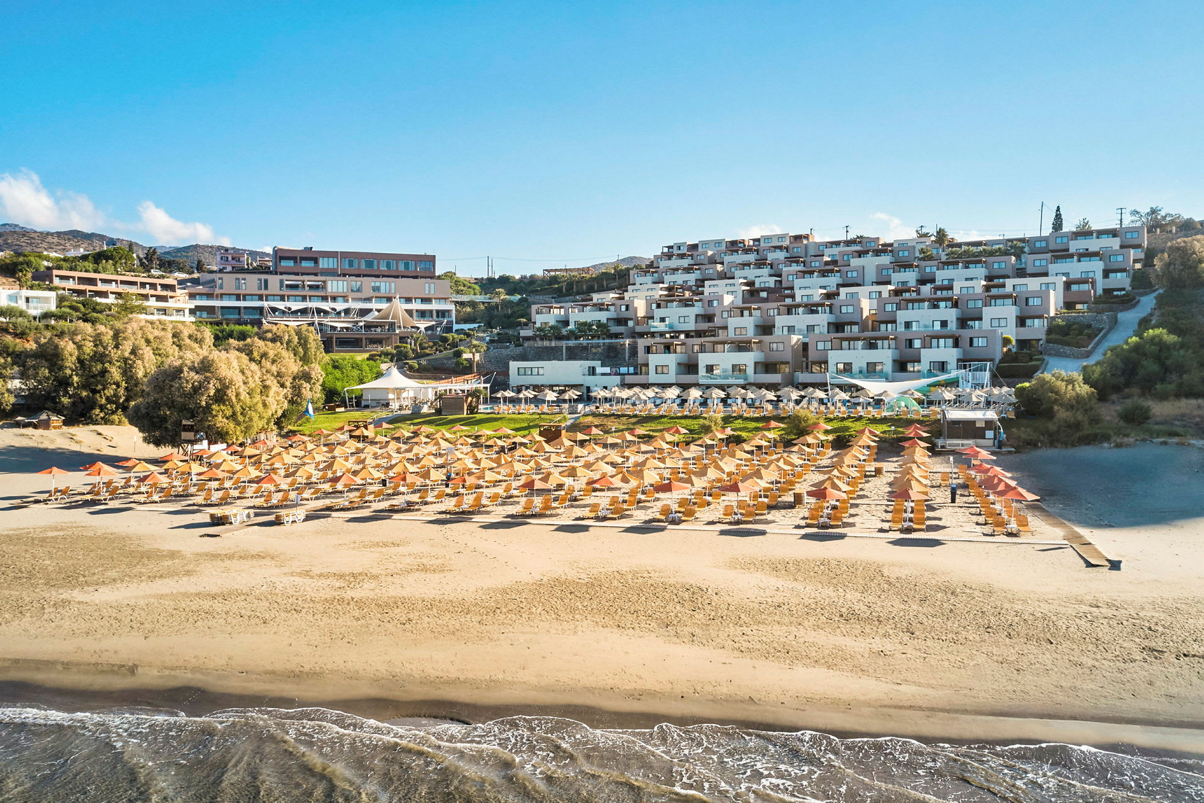 En sandstrand med solstolar och parasoller framför en resort med flera byggnader. (AI-genererad text)