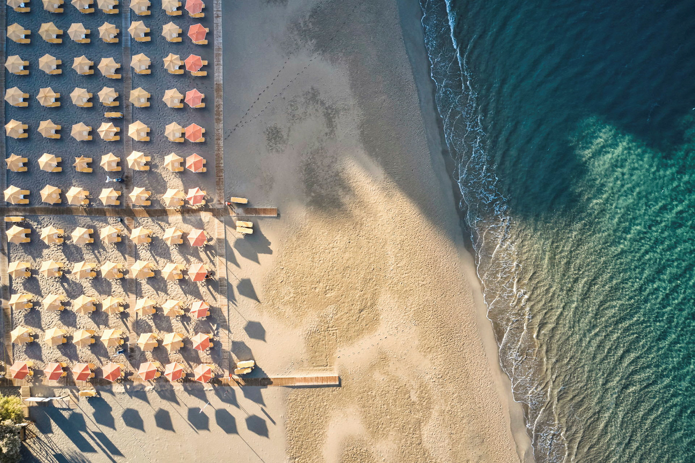 Flygfotografi av en strand med rader av parasoller och solstolar samt vågor som rullar in mot sanden. (AI-genererad text)