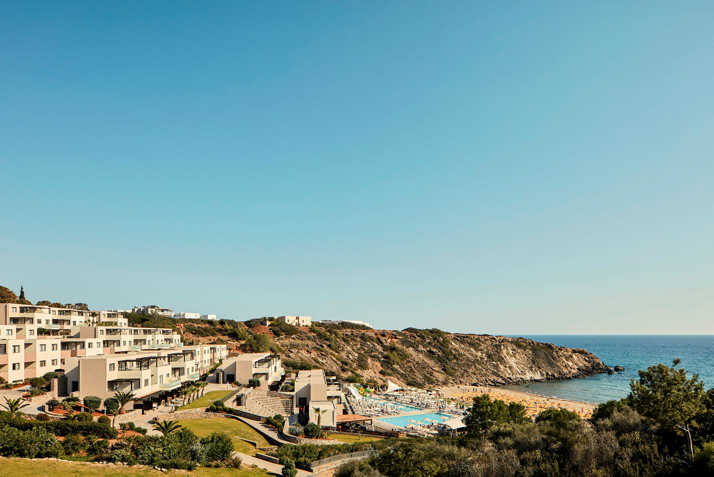 Hotellbyggnader nära en pool och en sandstrand bredvid havet. (AI-genererad text)