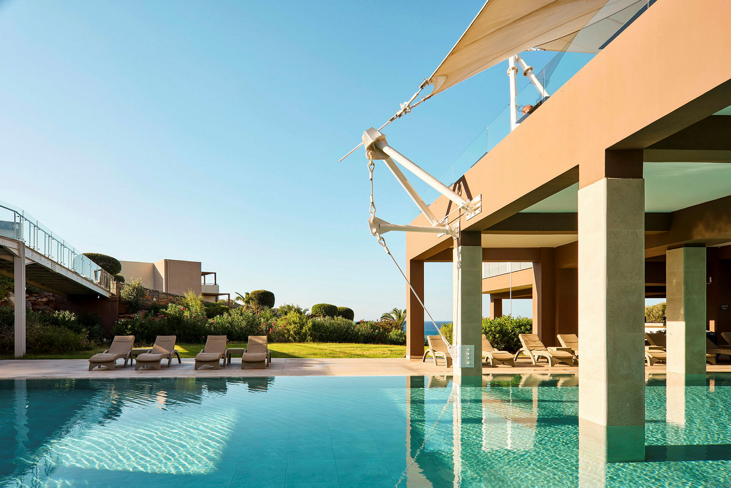 Modern byggnad med pool och solstolar, omgiven av grönska. (AI-genererad text)