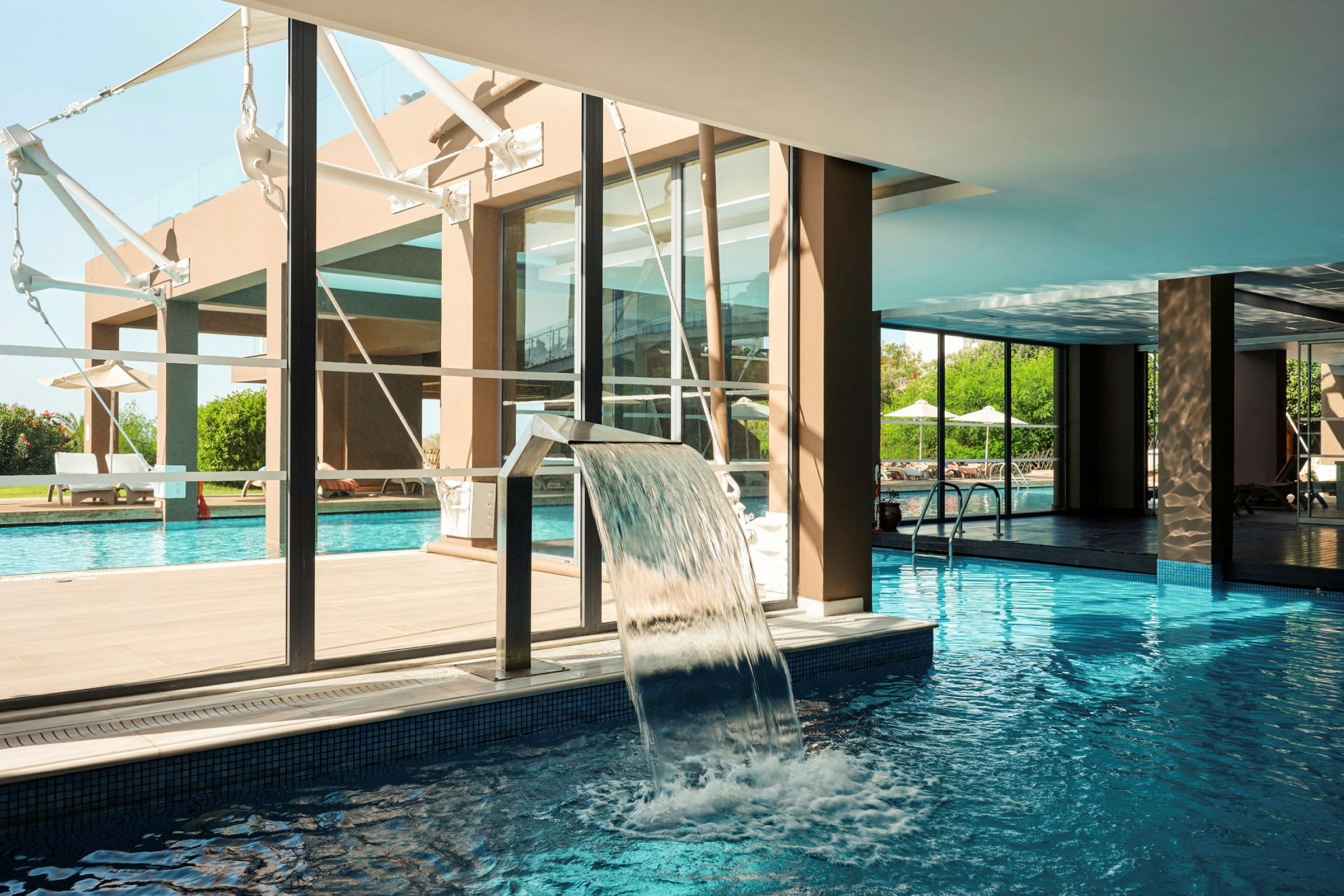 En pool med en vattenfontän och utsikt över solstolar utomhus. (AI-genererad text)